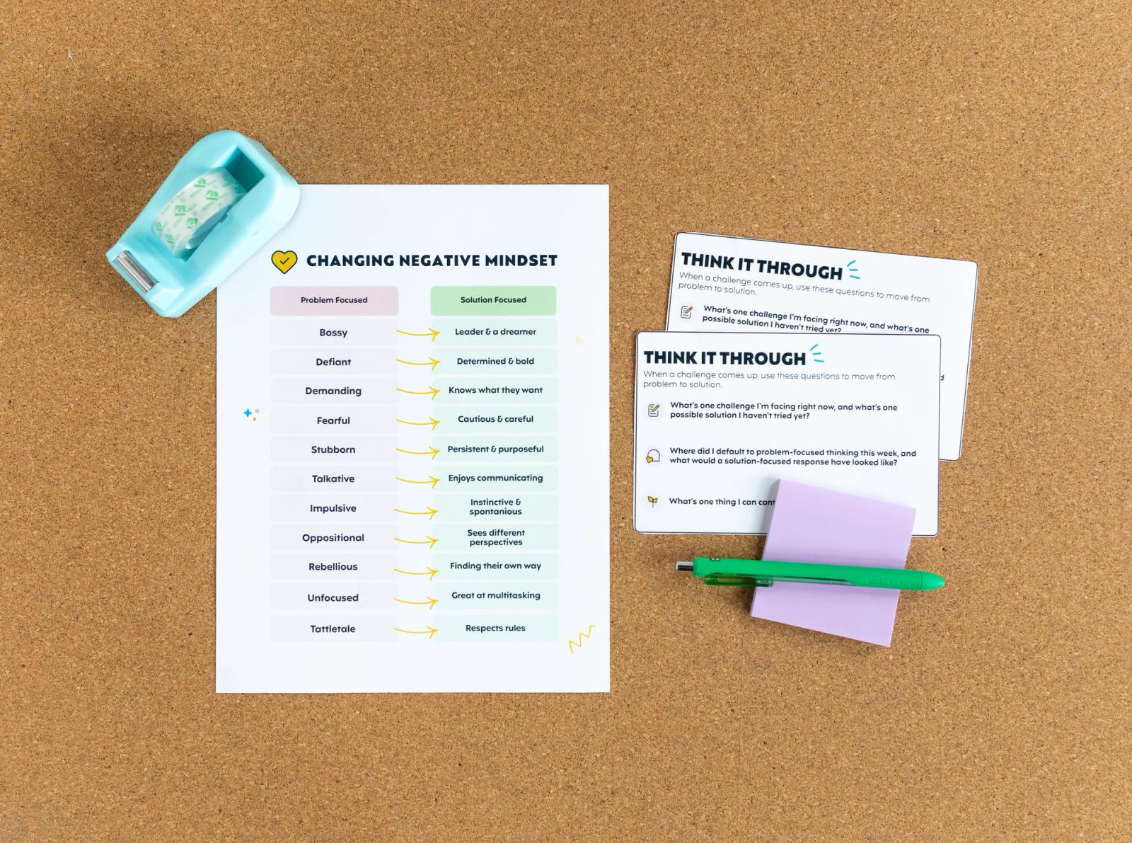 A piece of paper and two notecards lay on a corkboard. Purple sticky notes, a green pen, and blue tape dispenser lay around them.