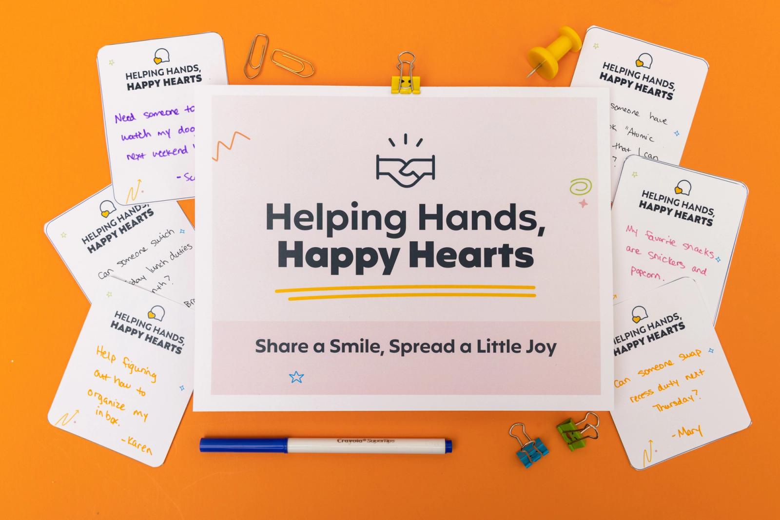 A poster that says "helping hands, happy hearts" with notecards, markers and paper clips scattered around it lays on an orange background.