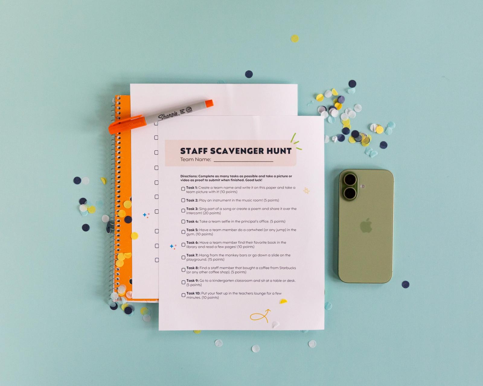 Sheets of paper, confetti, orange notebook, and a phone lay on a blue gray background.