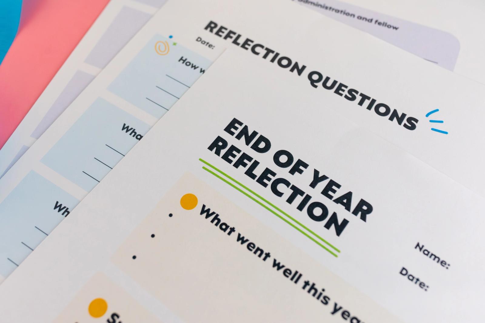 A close-up of a stack of papers. The top one says "end of year reflection."