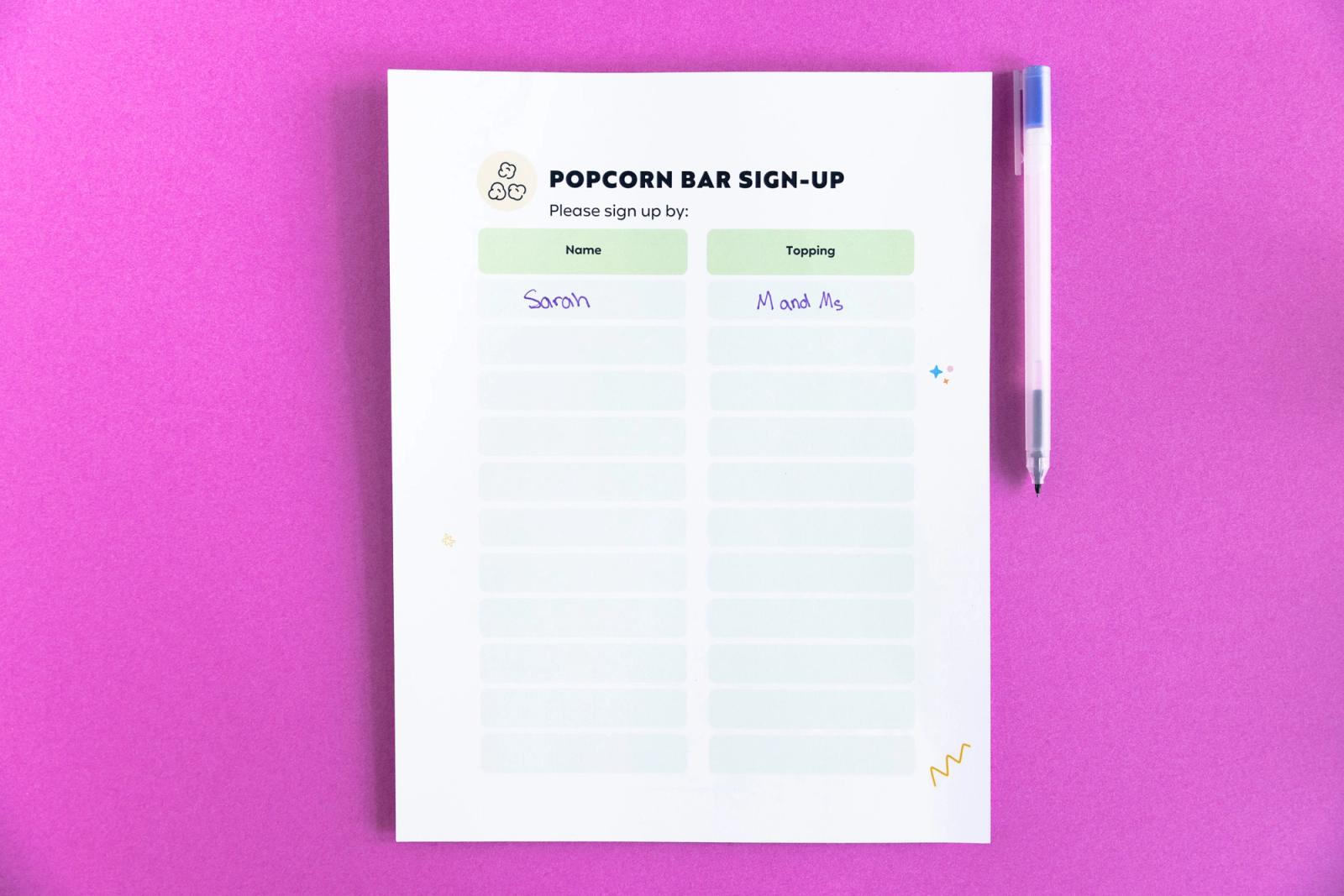 A poster that says "popcorn bar sign-up" and a pen lay on a magenta background.