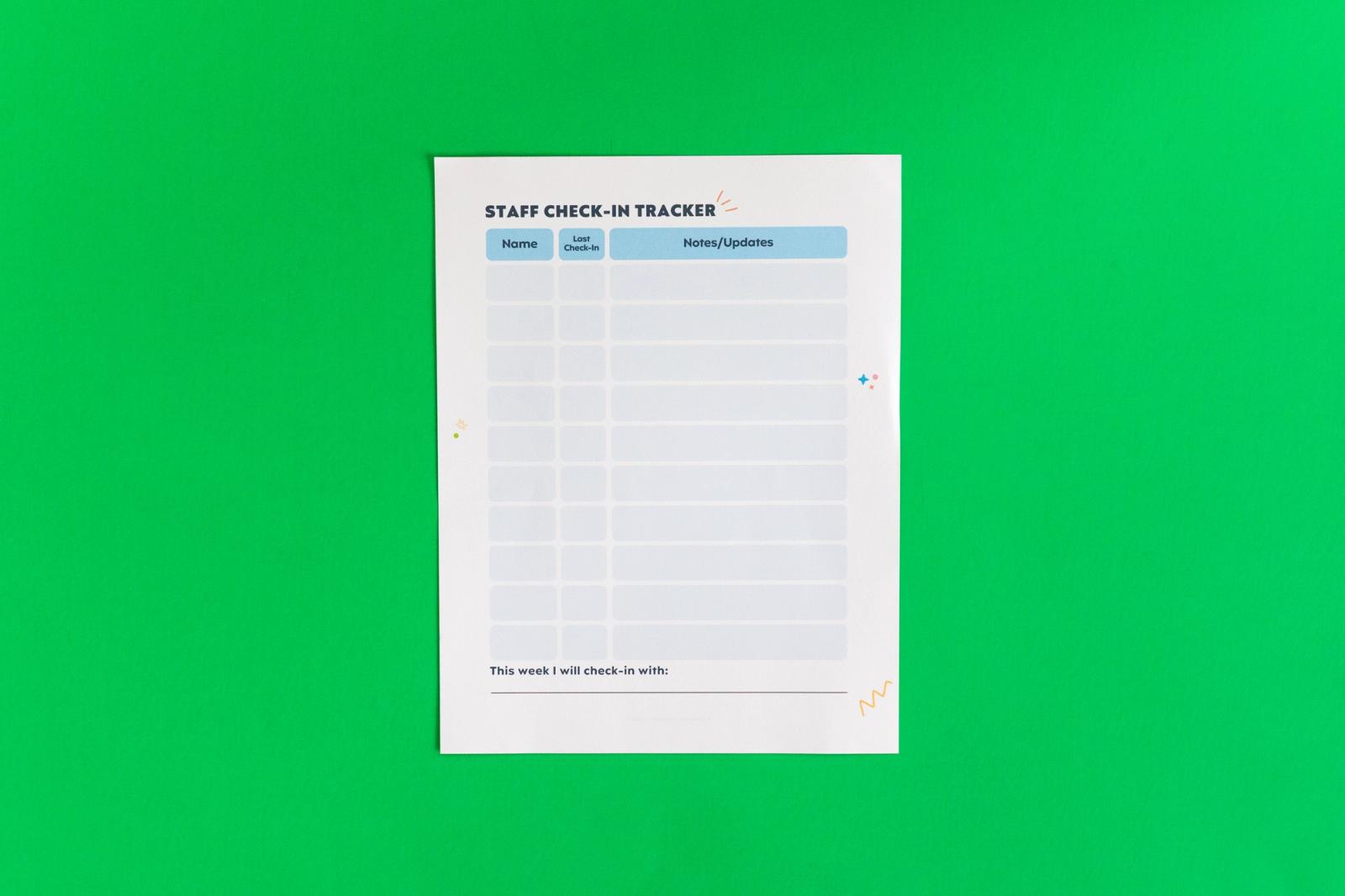 A sheet of paper that says "staff check-in tracker" is on a green background.