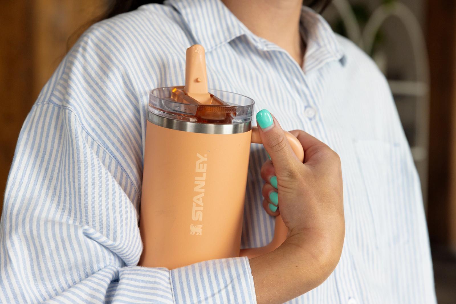 Someone holds a peach water bottle in their hands.