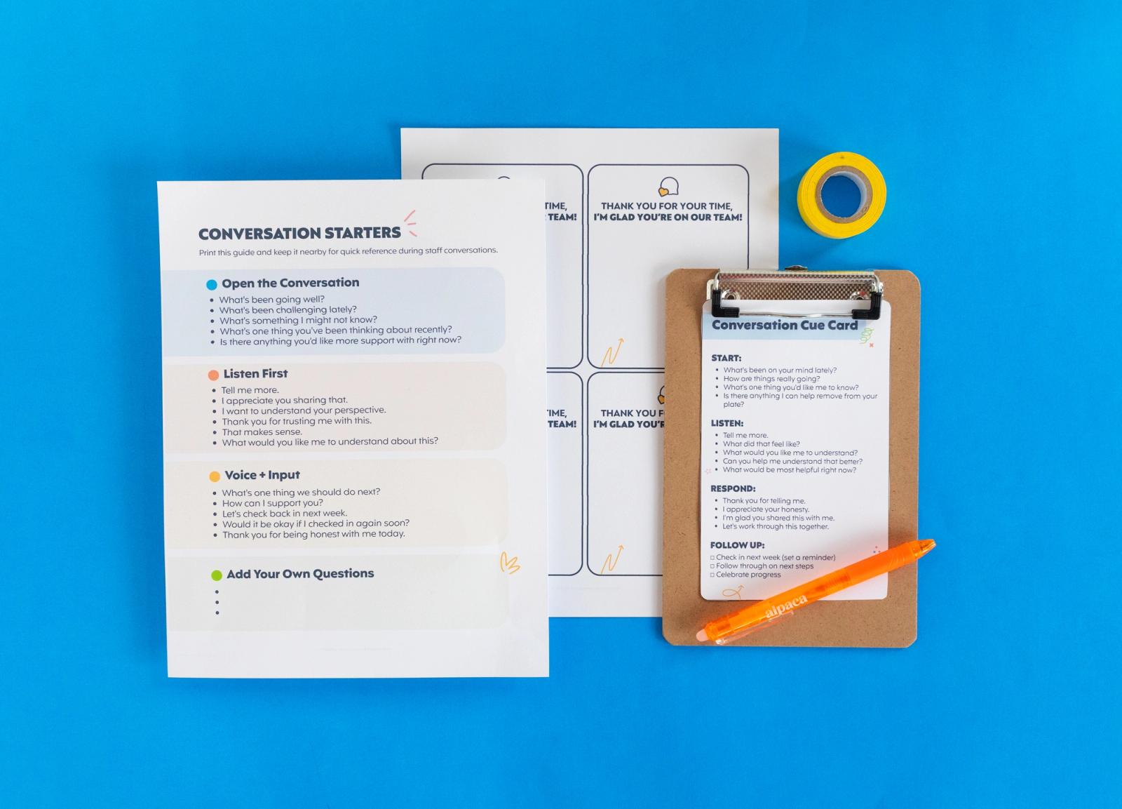 Two sheets of paper, small clipboard, roll of tape, and orange pen lay on a light blue background.