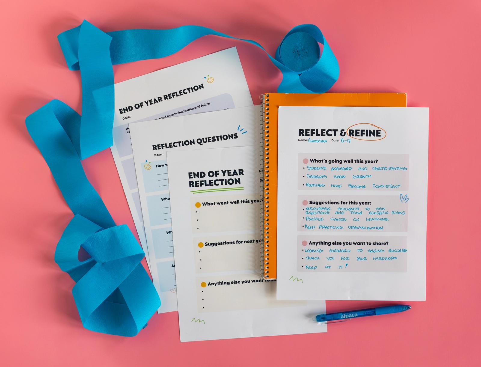 Sheets of paper, an orange notebook, and a blue pen lay on a pink background. Blue streamers surround them.