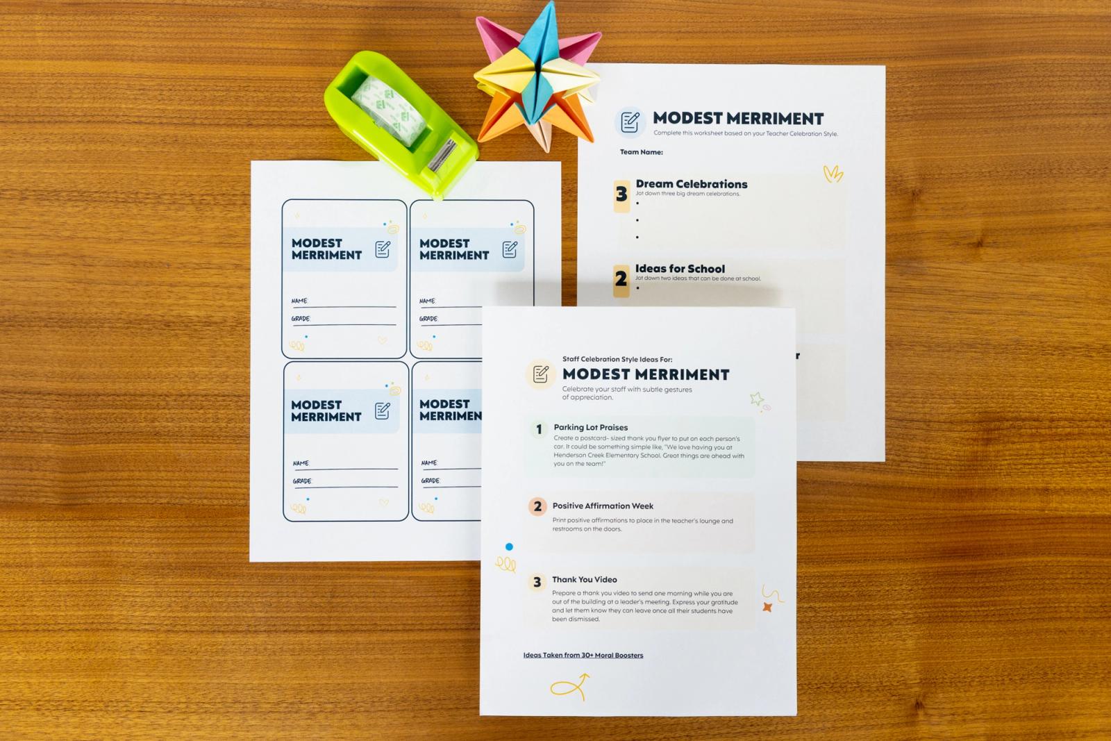 Three sheets of paper that say "modest merriment," tape, and star decoration lay on a table.