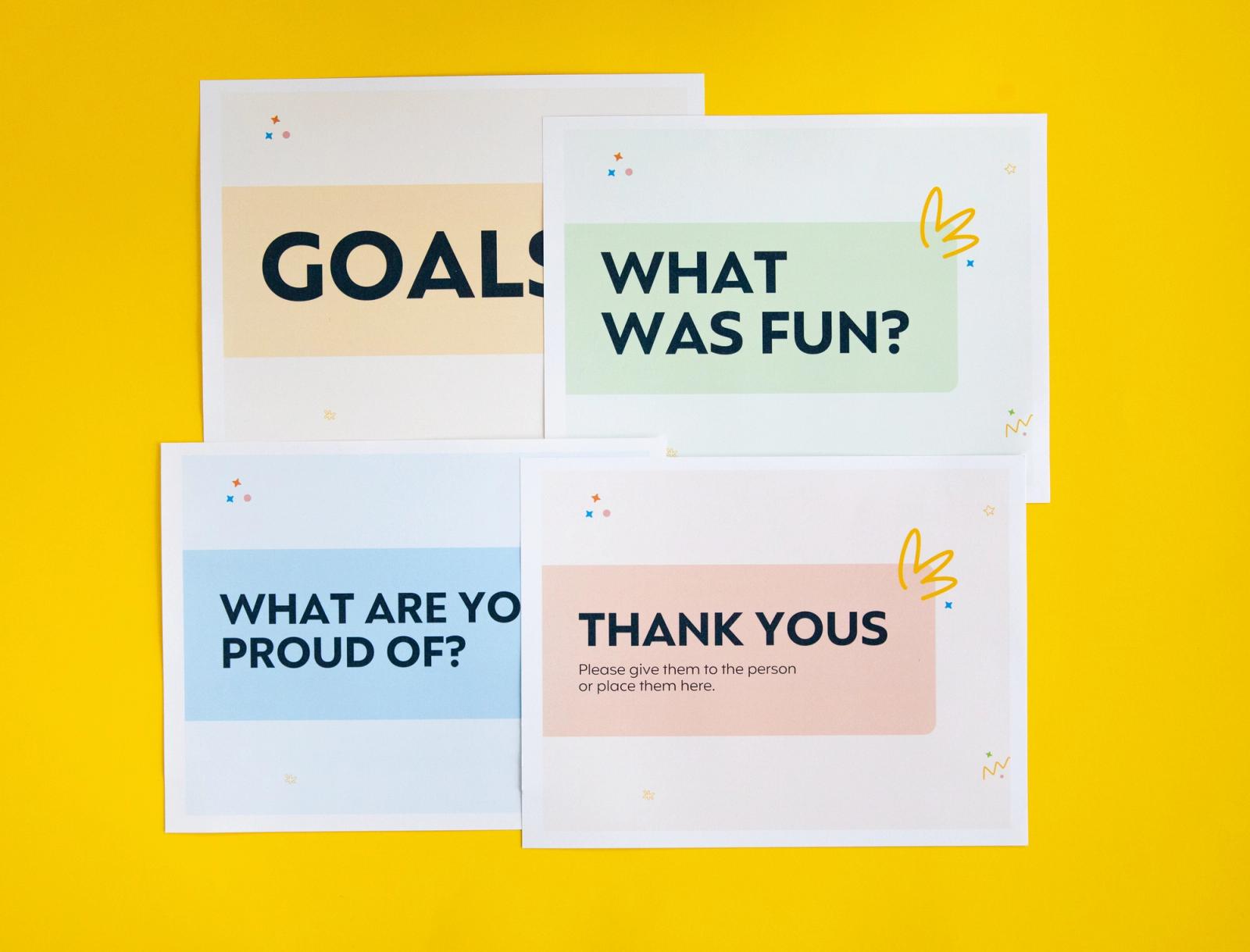 Four posters that say "goals," "what was fun?" "what are you proud of?" and "thank yous"lay on a yellow background.