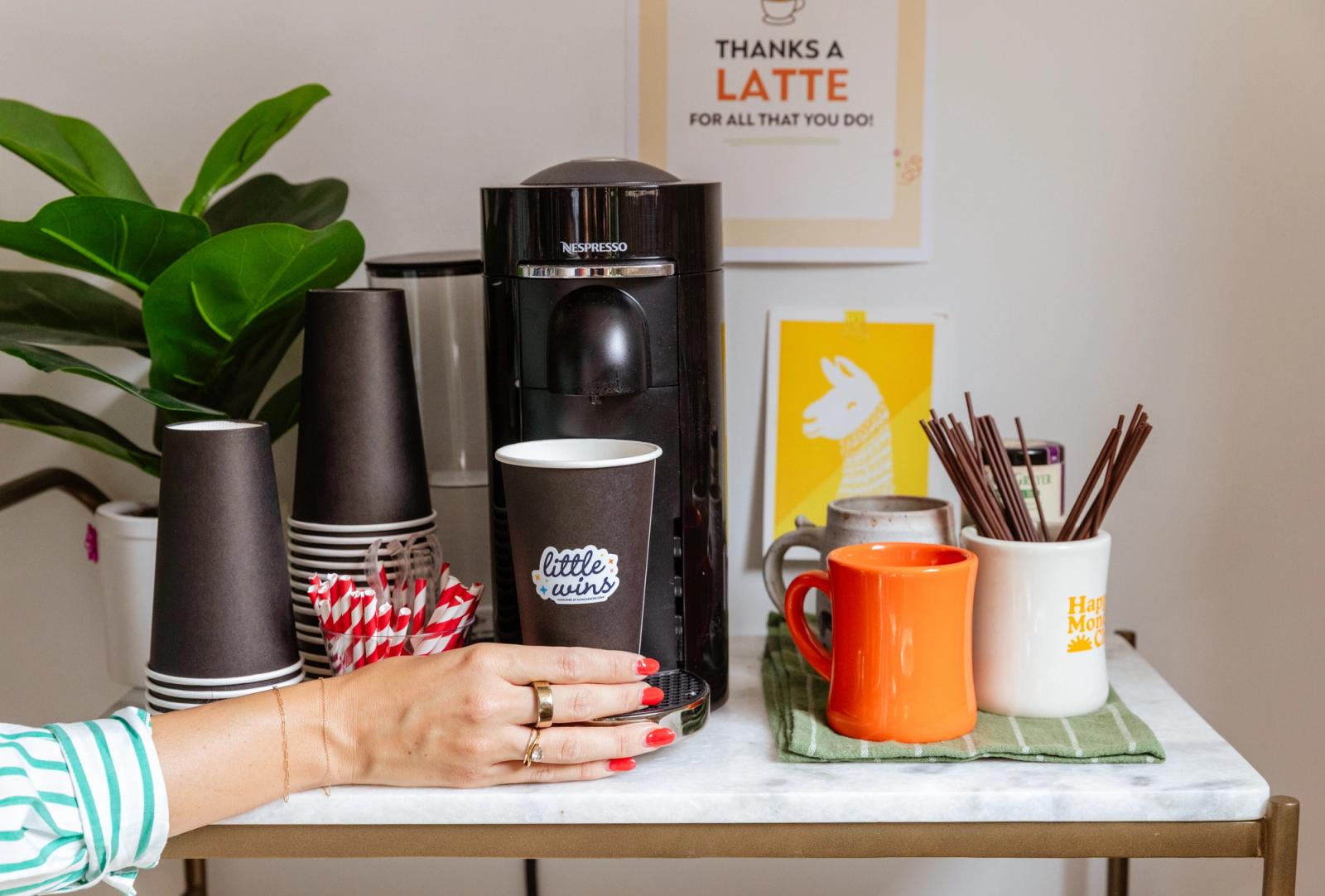 A hand reaches in to grab a to-go coffee cup from a coffee station.