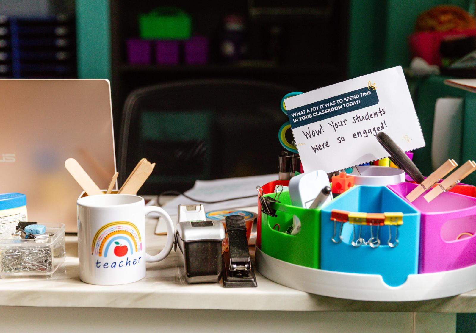 A handwritten note sits in a pencil holder on a teacher's desk. 