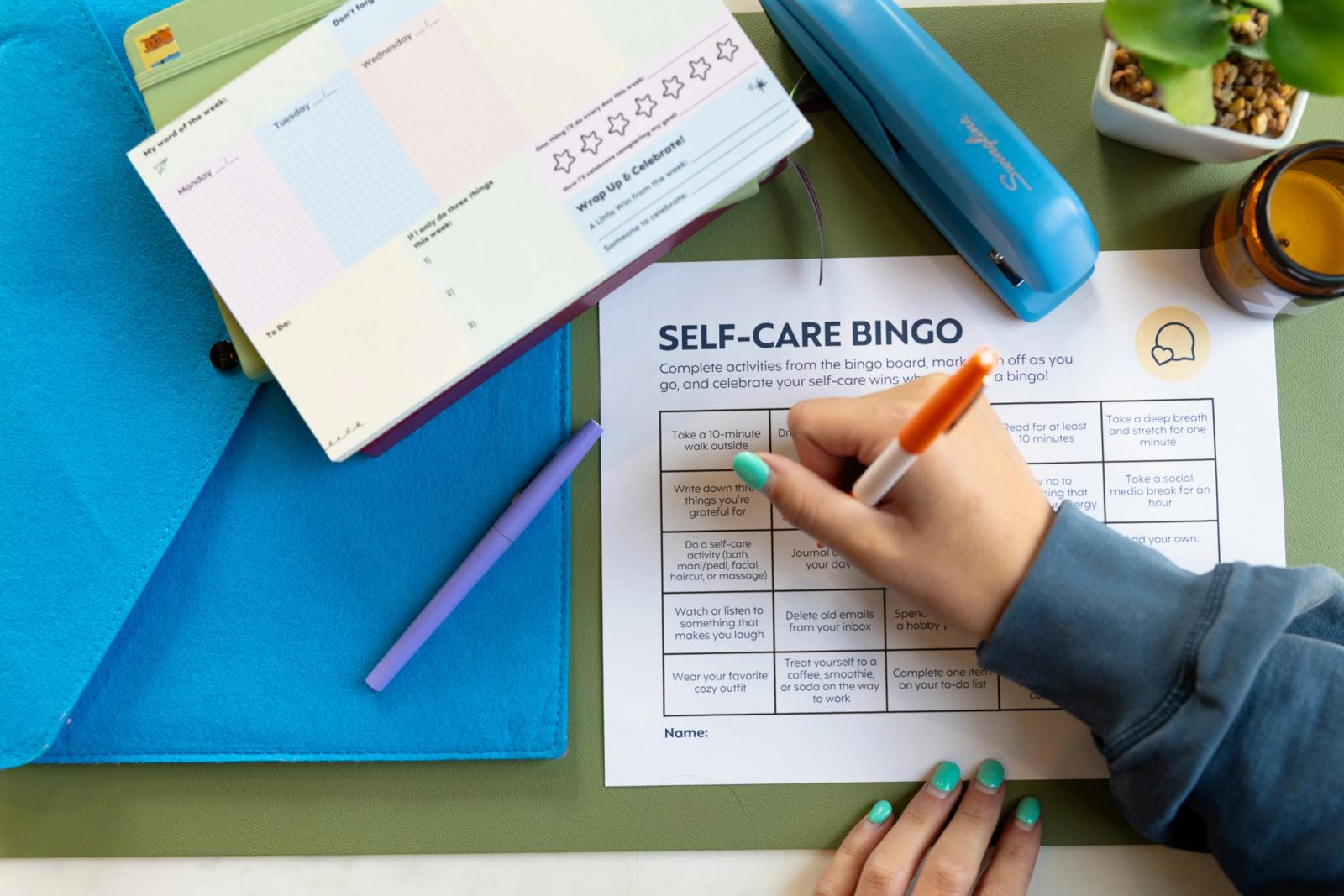 A hand reaches in and completes a bingo sheet that is on a desk.