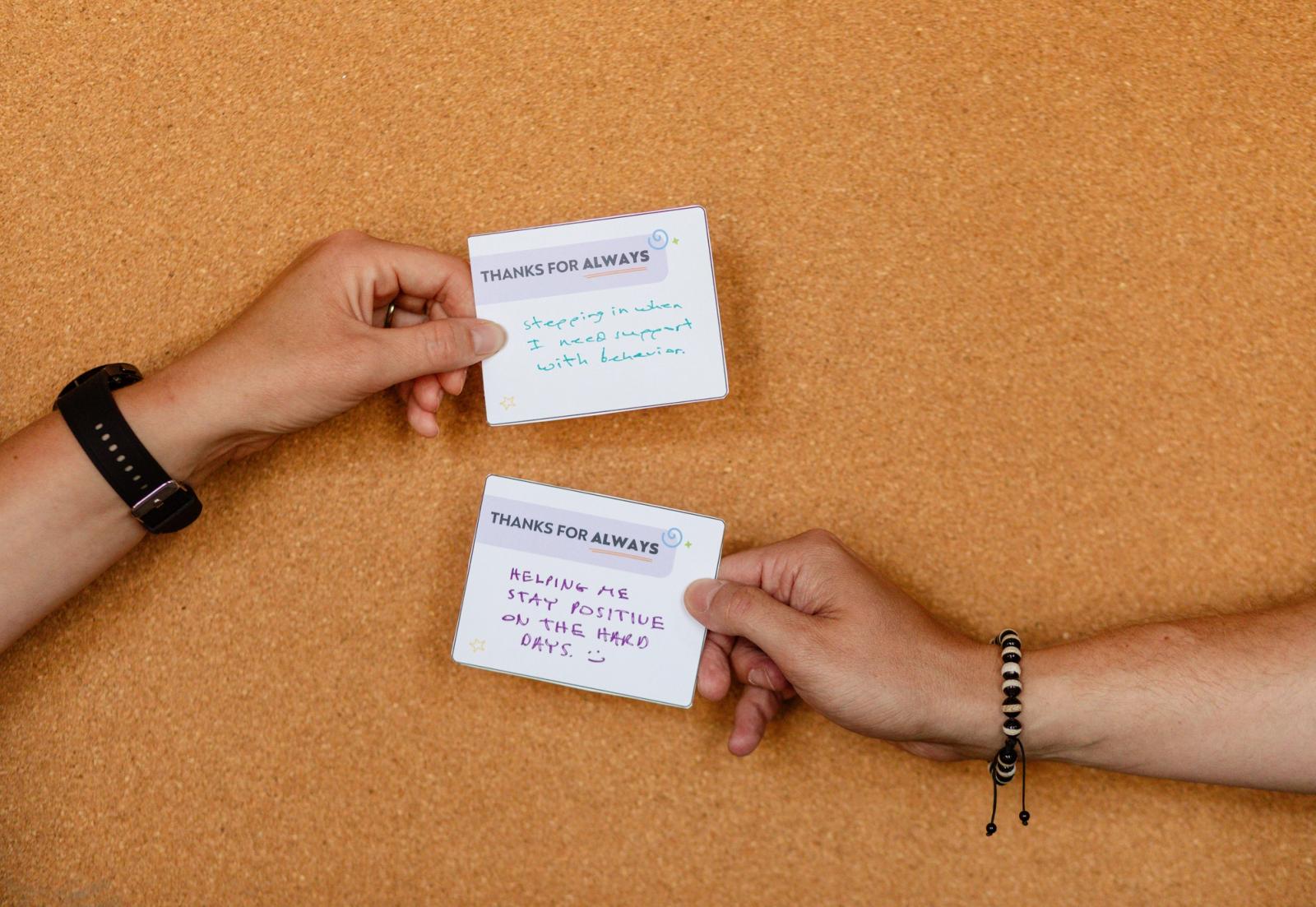 Two handsexchange handwritten notes in front of a cork board background.
