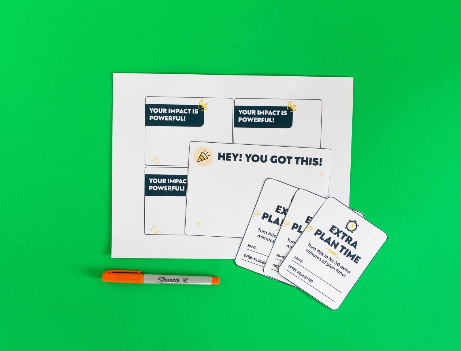 A sheet of paper, small notecards, and an orange pen lays on a green background.