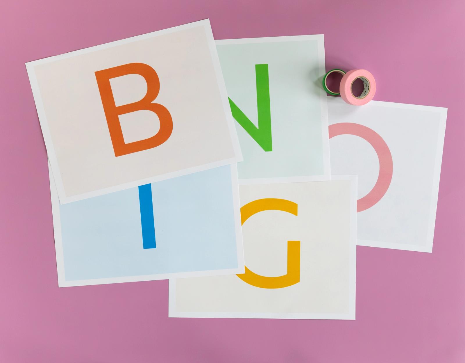 Sheets of paper, each with one letter on them, lay on a pink background. 