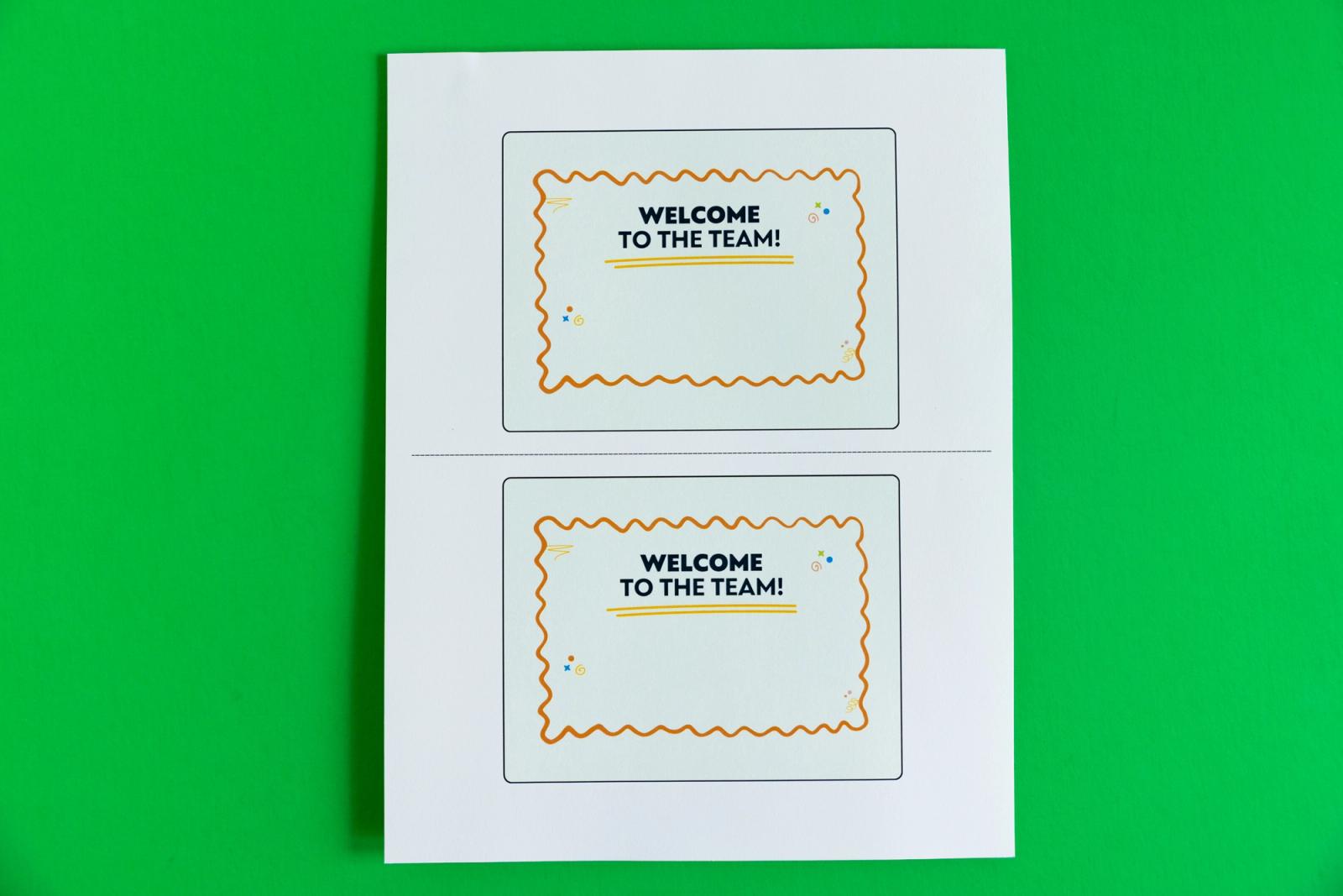 Sheet of paper with two postcards that say "welcome to the team" lay on a green background.