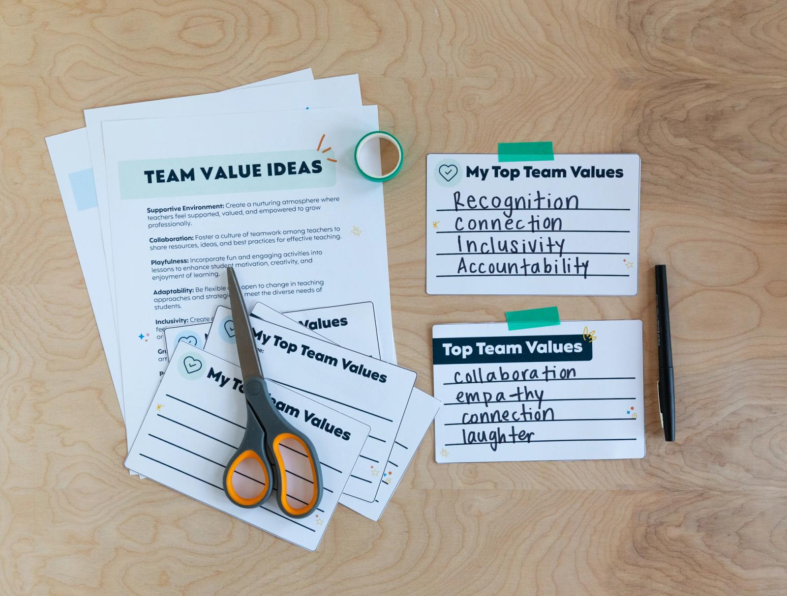 A pile of papers, handwritten notecards lay on a wood background. A pair of scissors, tape, and black pen lay next to the papers.