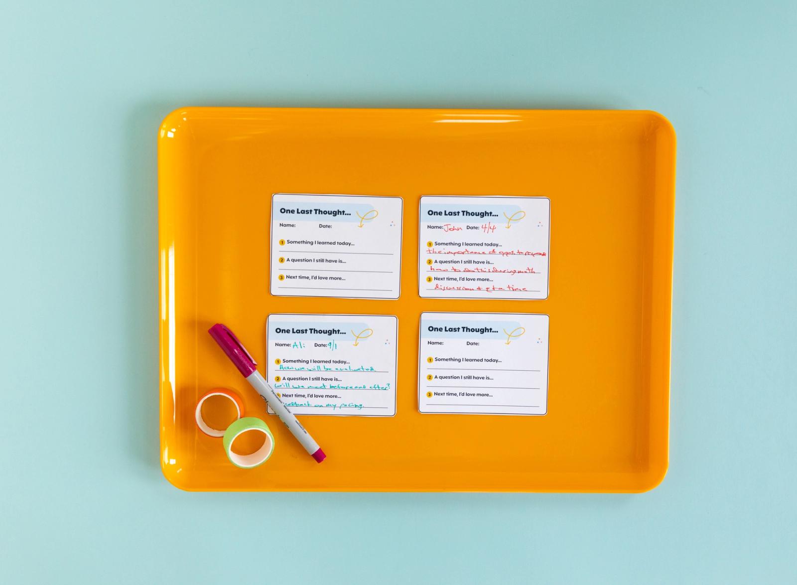 Four small sheets of paper with handwritten notes, a pen, and rolls of tape lay on an orange tray. The tray is on a light blue background. 