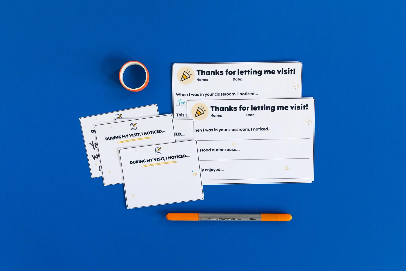 Five small notecards on a blue background with a roll of tape and orange pencil around them.