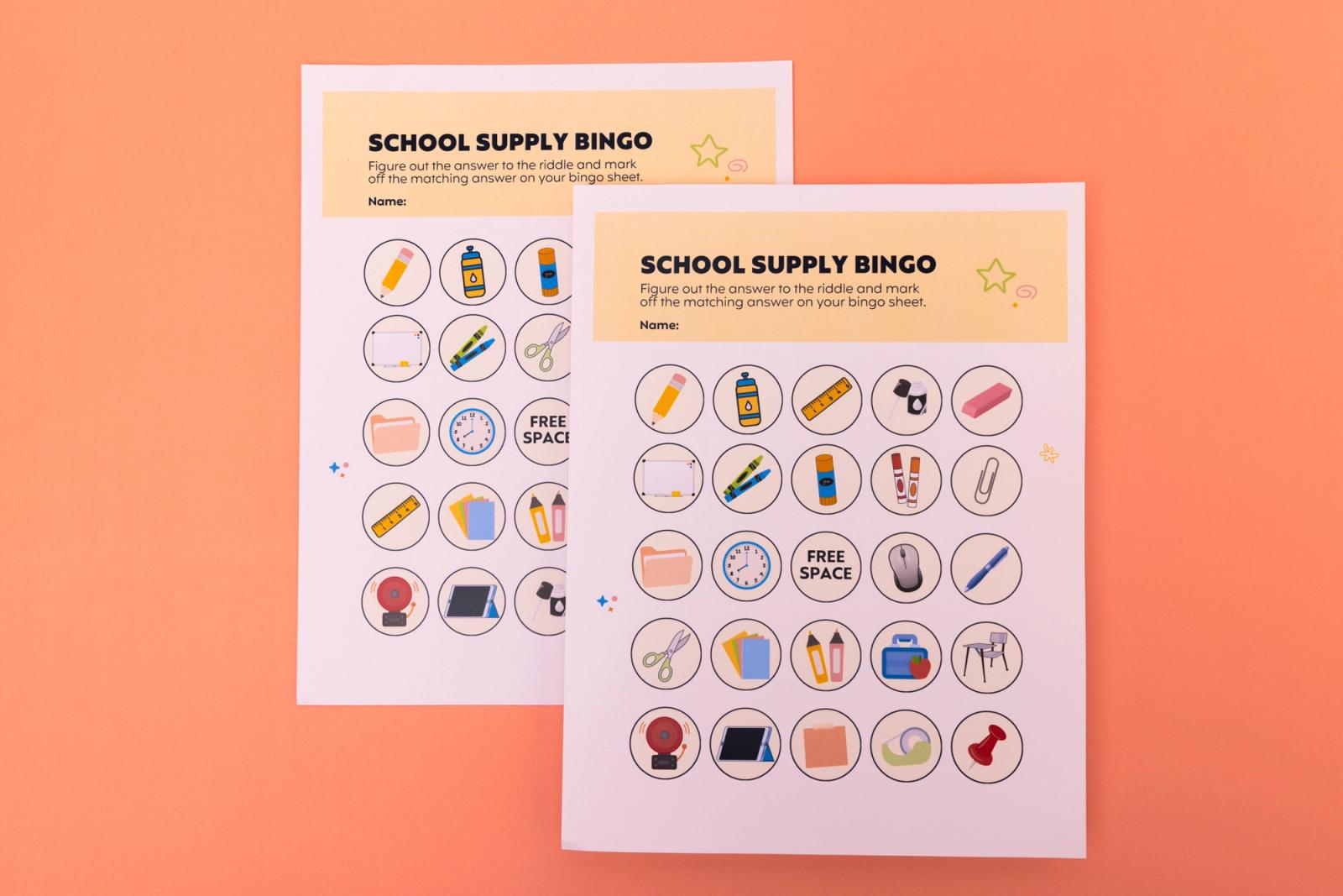 Two bingo sheets with pictures of school supplies lay on a pink background.