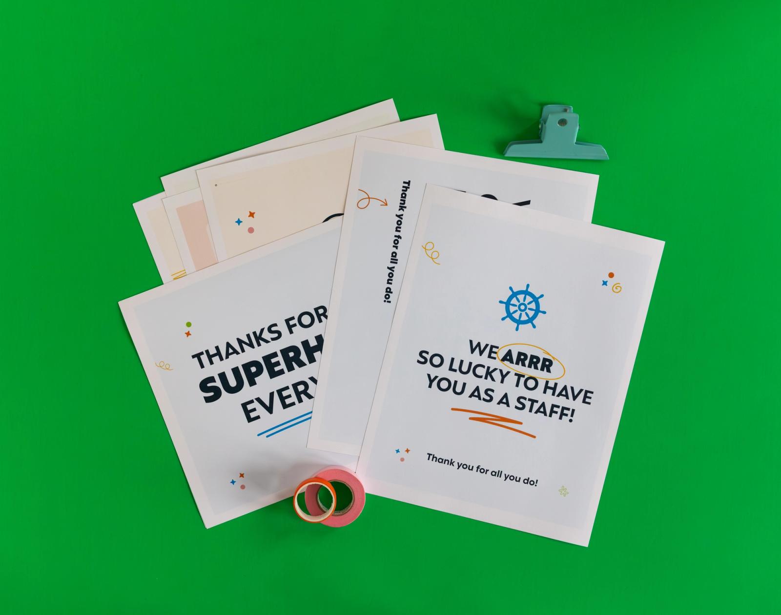 Several posters lay on a green background. Rolls of tape and clips surround them. 