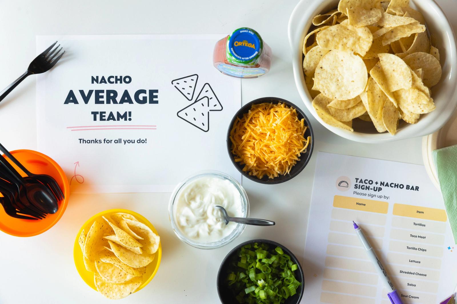 Two sheets of paper lay on a white table. Small bowls of nacho ingredients lay around them.