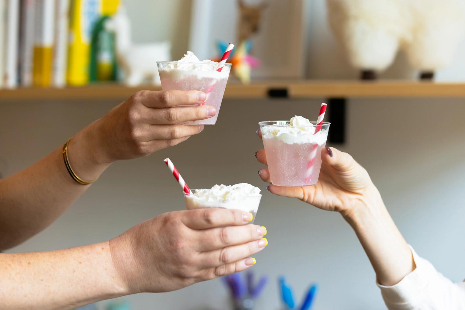 Three hands reach in to clink glasses that have an Italian ice drink in them.