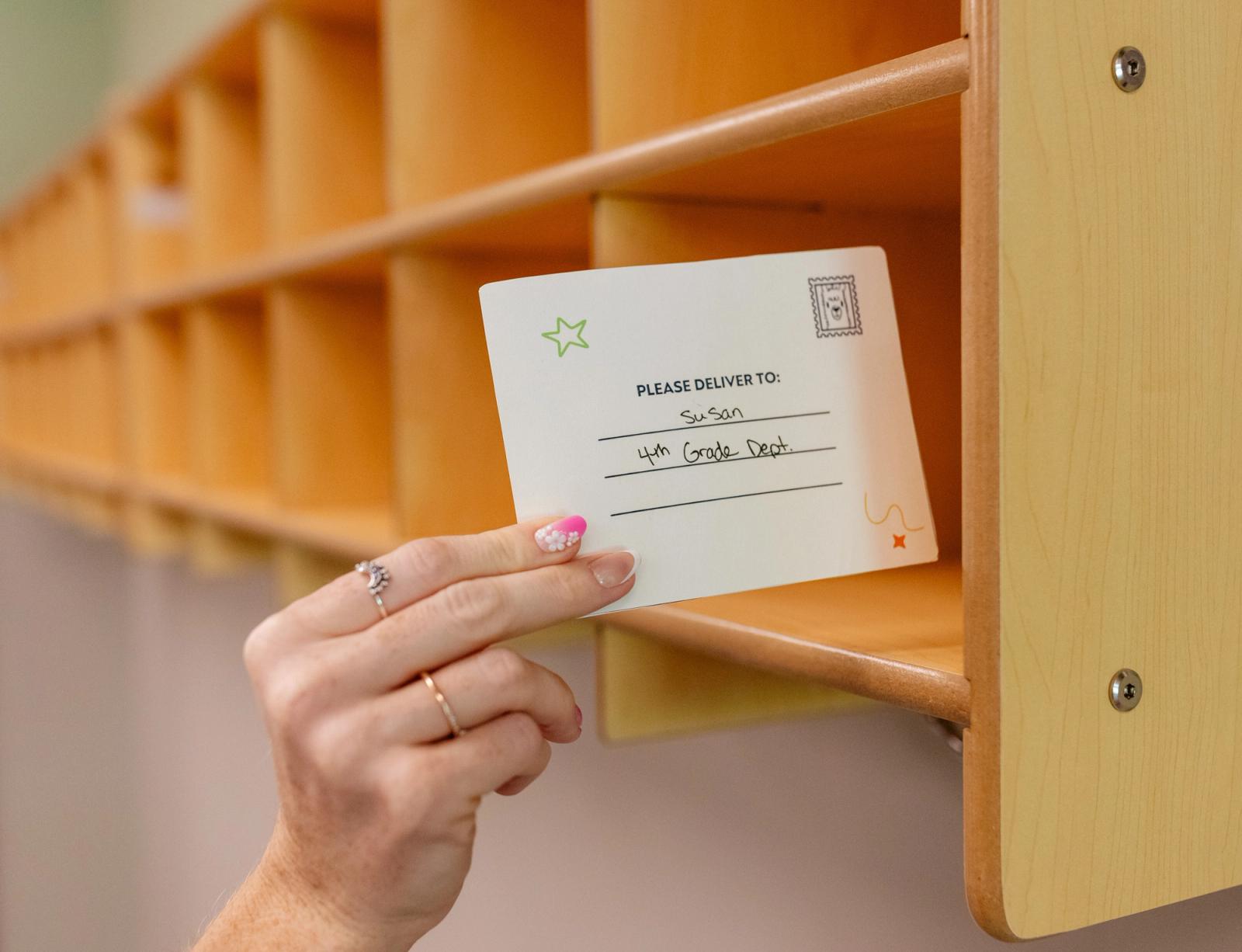 A hand places a postcard into a cubby.