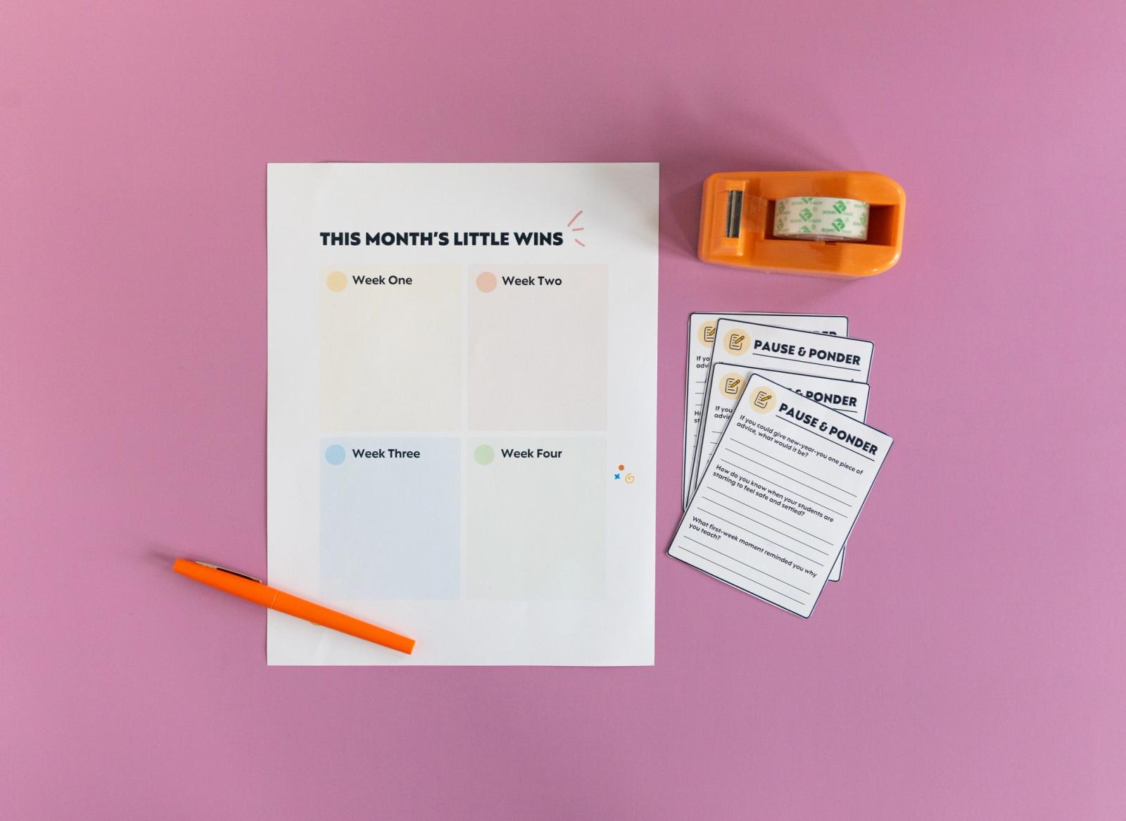 A paper with a grid on it and an orange pen beside it lay on a pink background. Blank notes and an orange tape dispenser lay next to it.