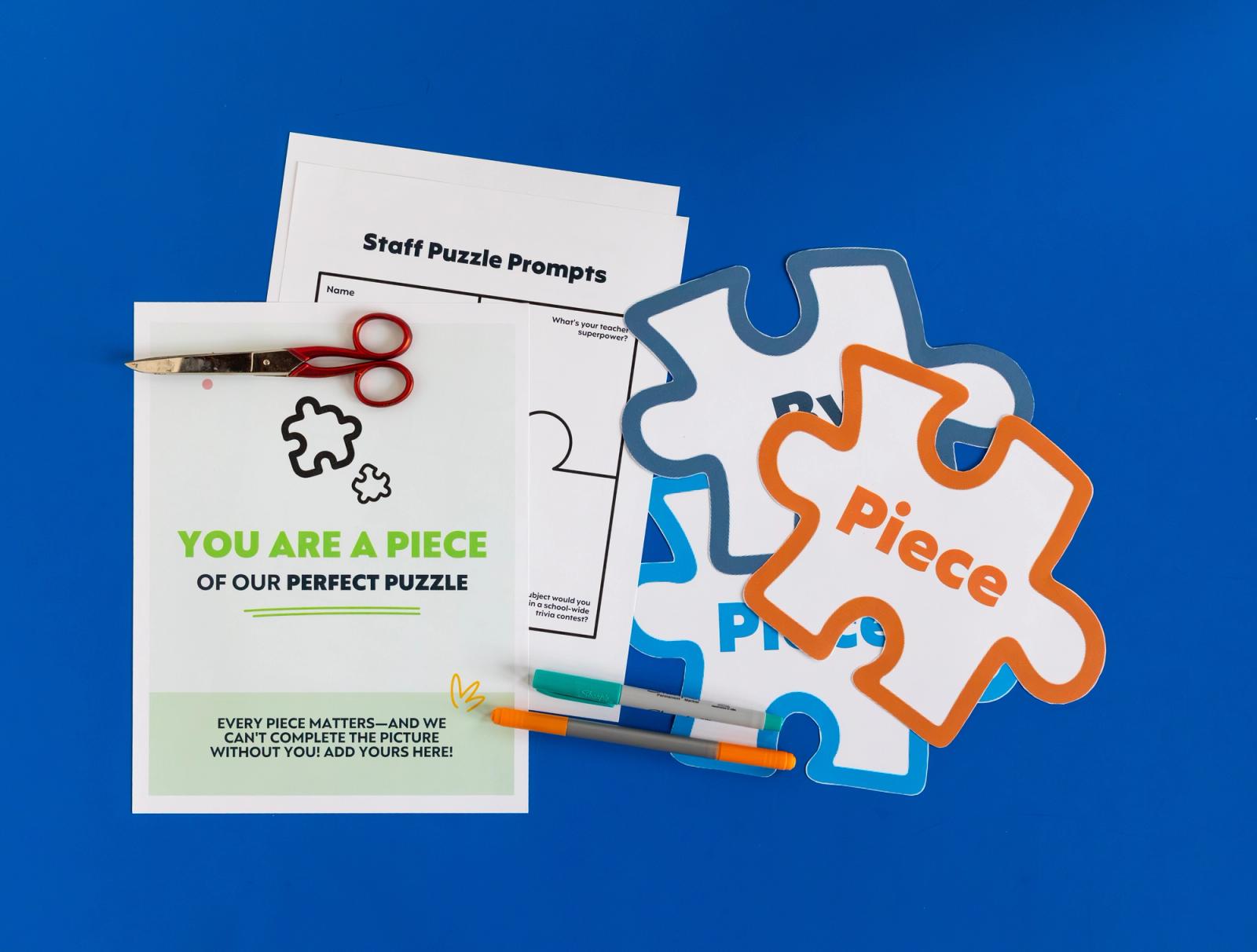 Cut-out puzzle pieces, sheets of paper, scissors, and pens lay on a dark blue background.