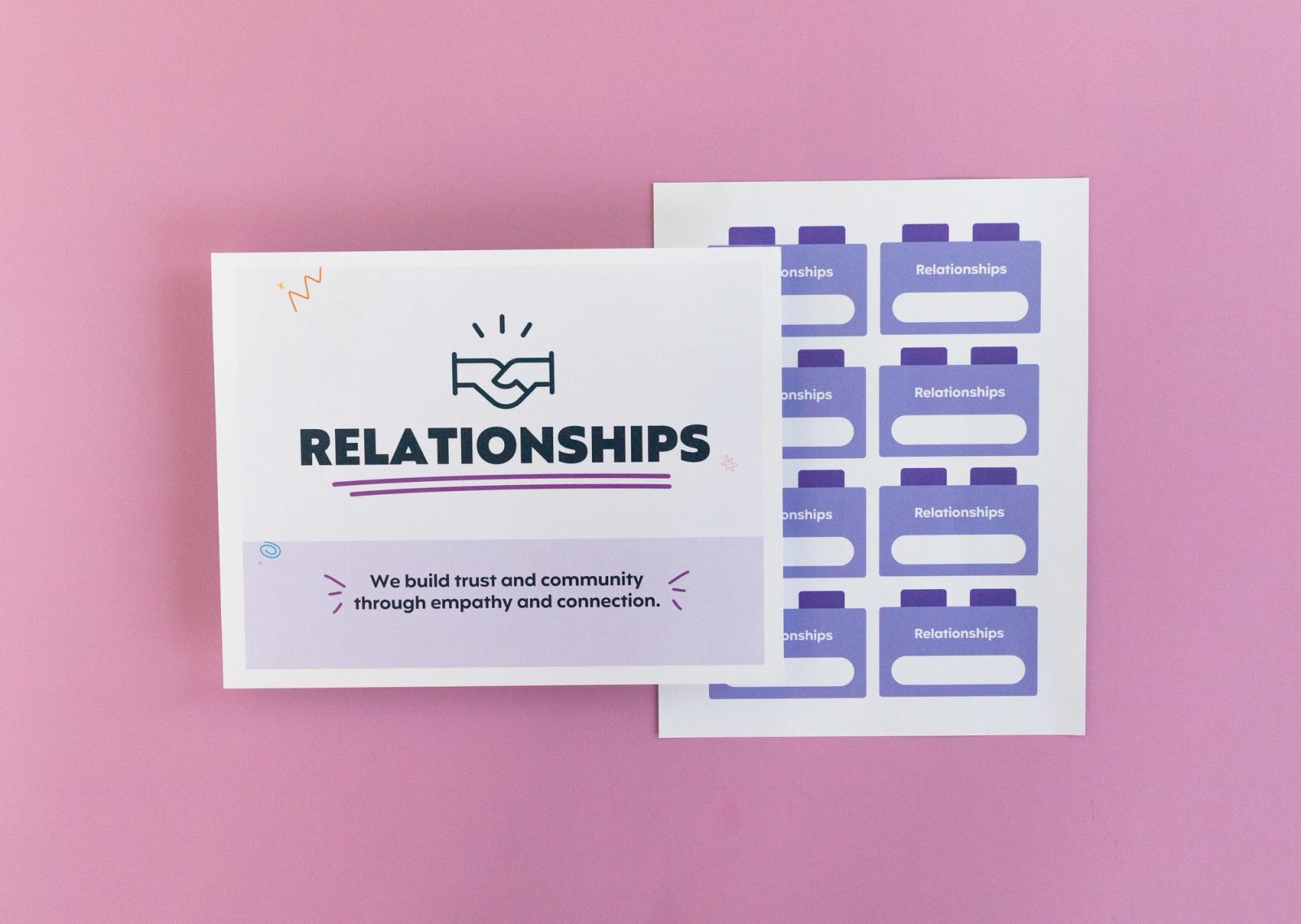 Sheet of paper that says "relationships" and another with small squares on it lay on a pink background.