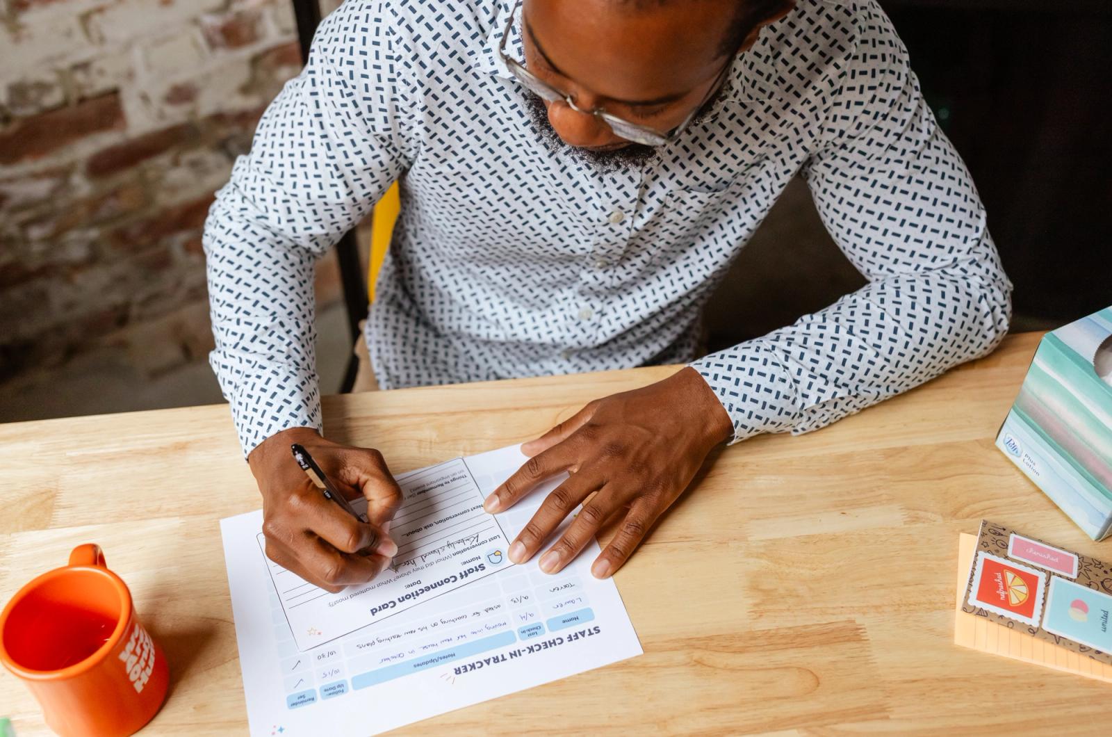 A man sits at a desk writing on a sheet of paper. 
