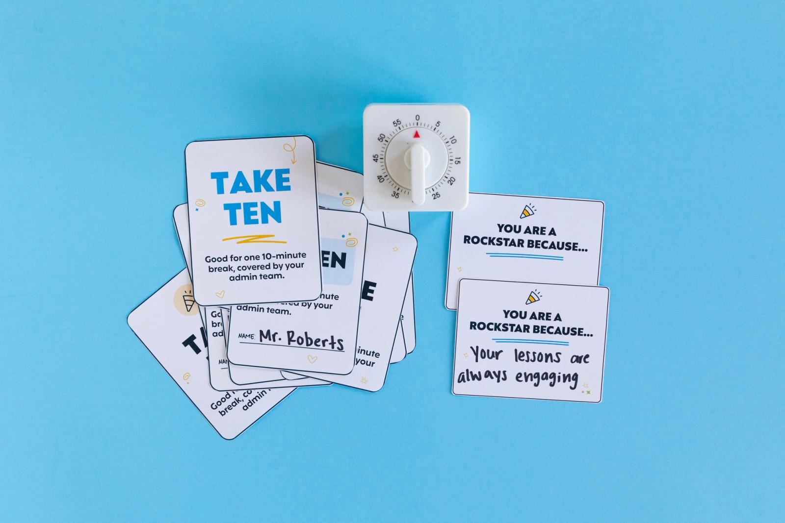 A group of small pieces of paper lay on a light blue background. A white timer lays next to them, all on a light blue background.