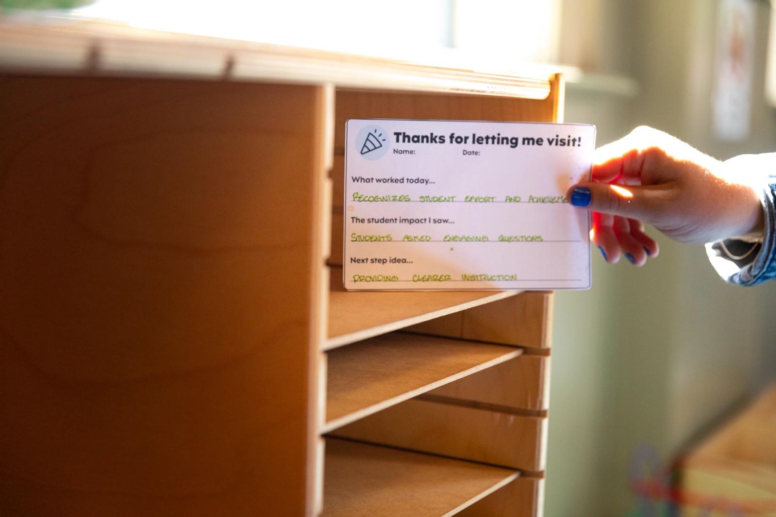 A hand places a small notecard in a mailbox slot.