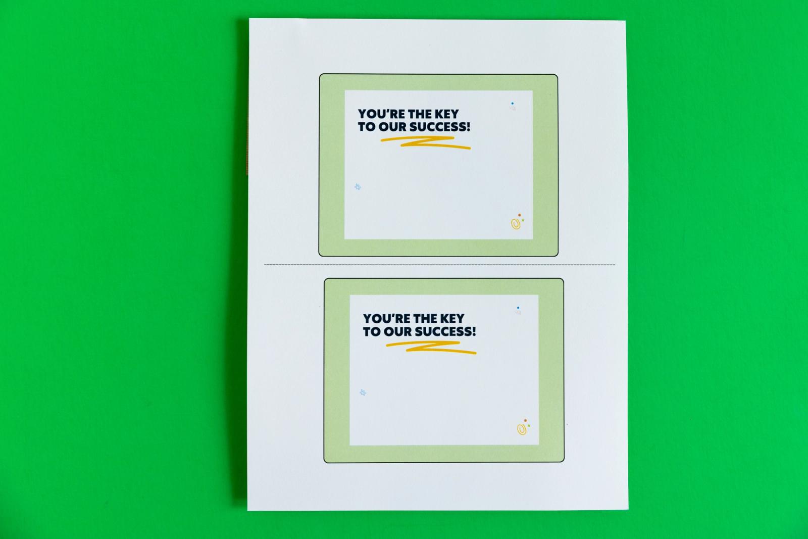 Sheet of paper with two postcards that say "you're the key to our success" lay on a green background.