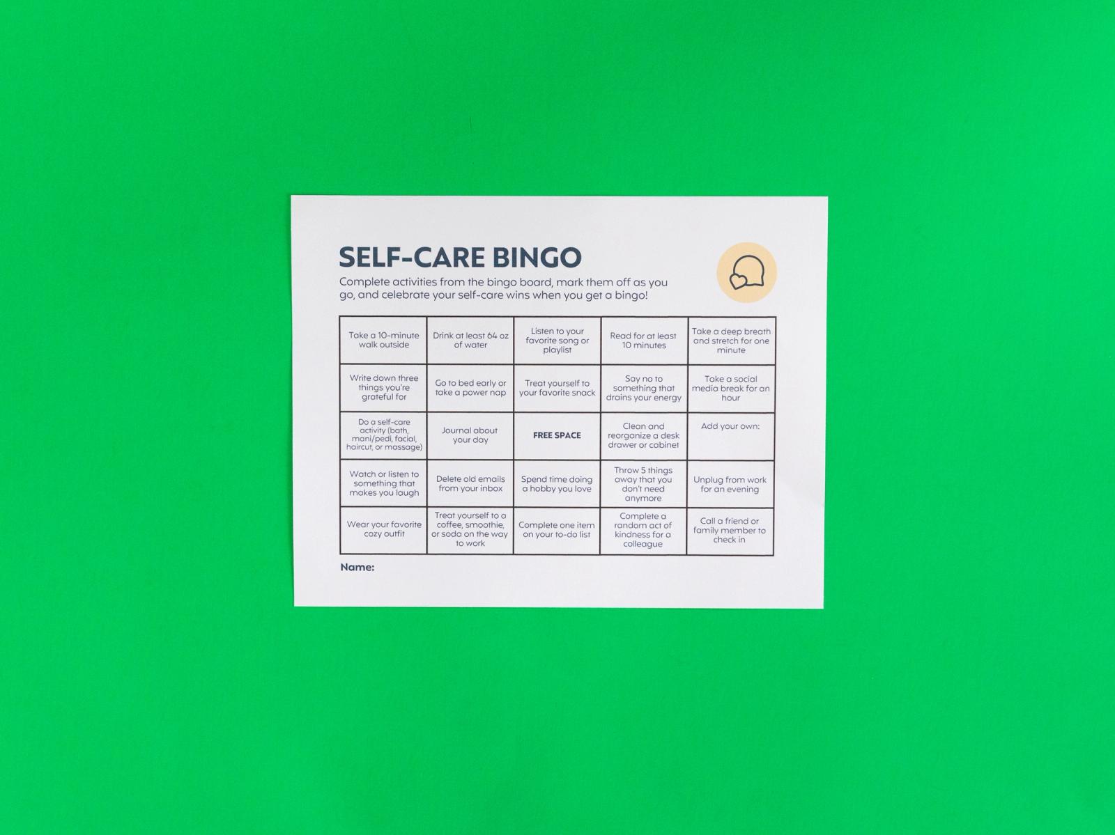 A sheet of paper that says "self-care bingo" lays on a green background.