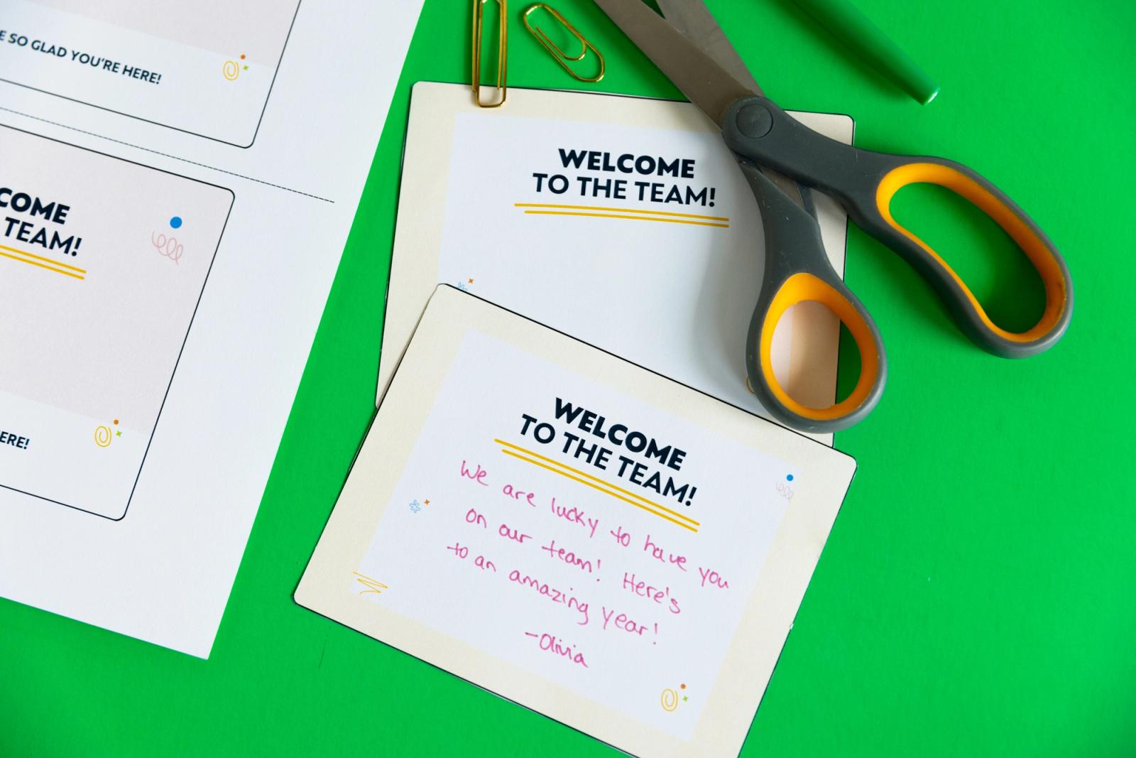 A notecard with a written note, scissor, and paper clips lay on a green background.