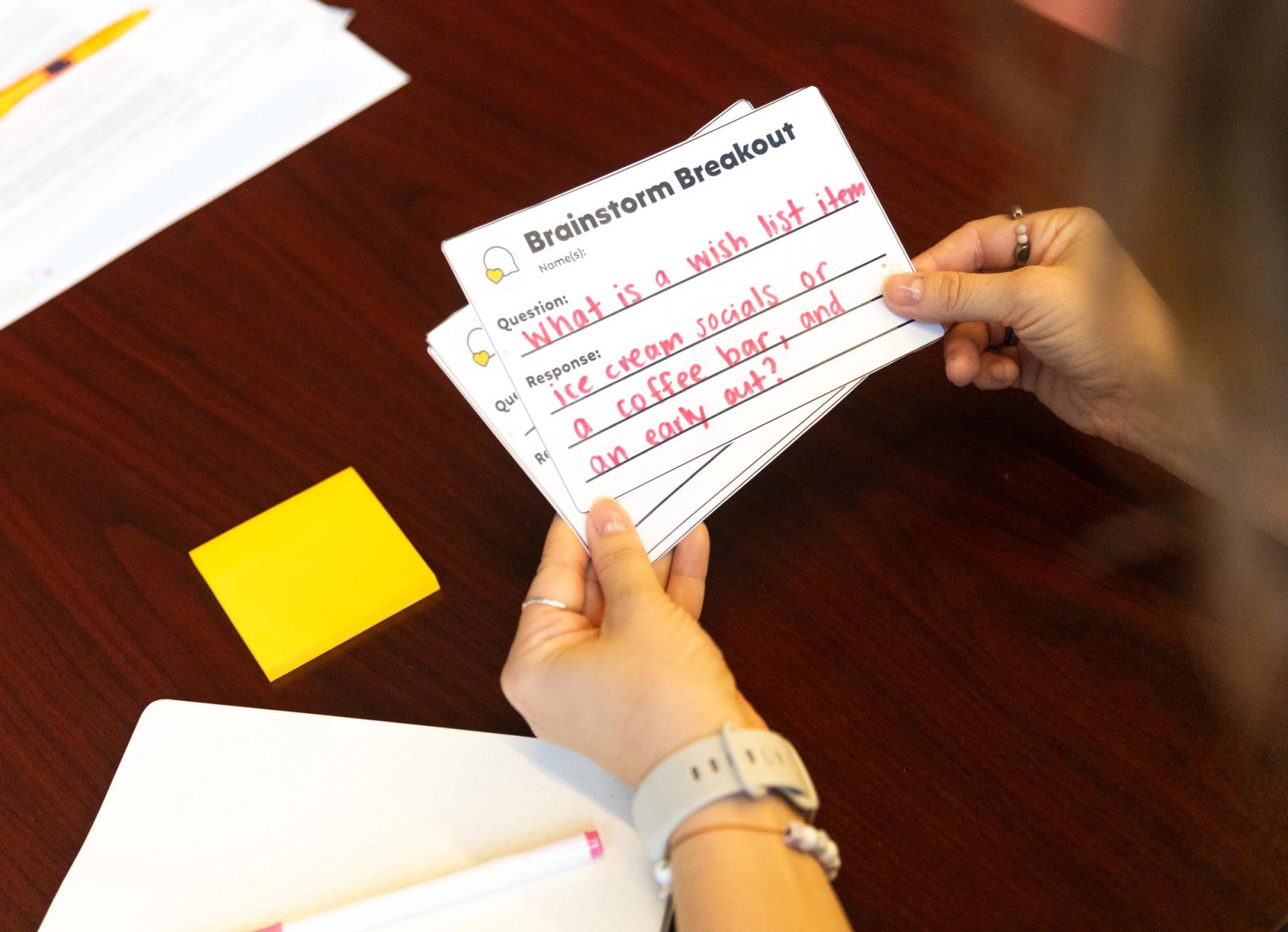 Hands shuffle through notecards that say "brainstorm breakout" on them while sitting at a table.