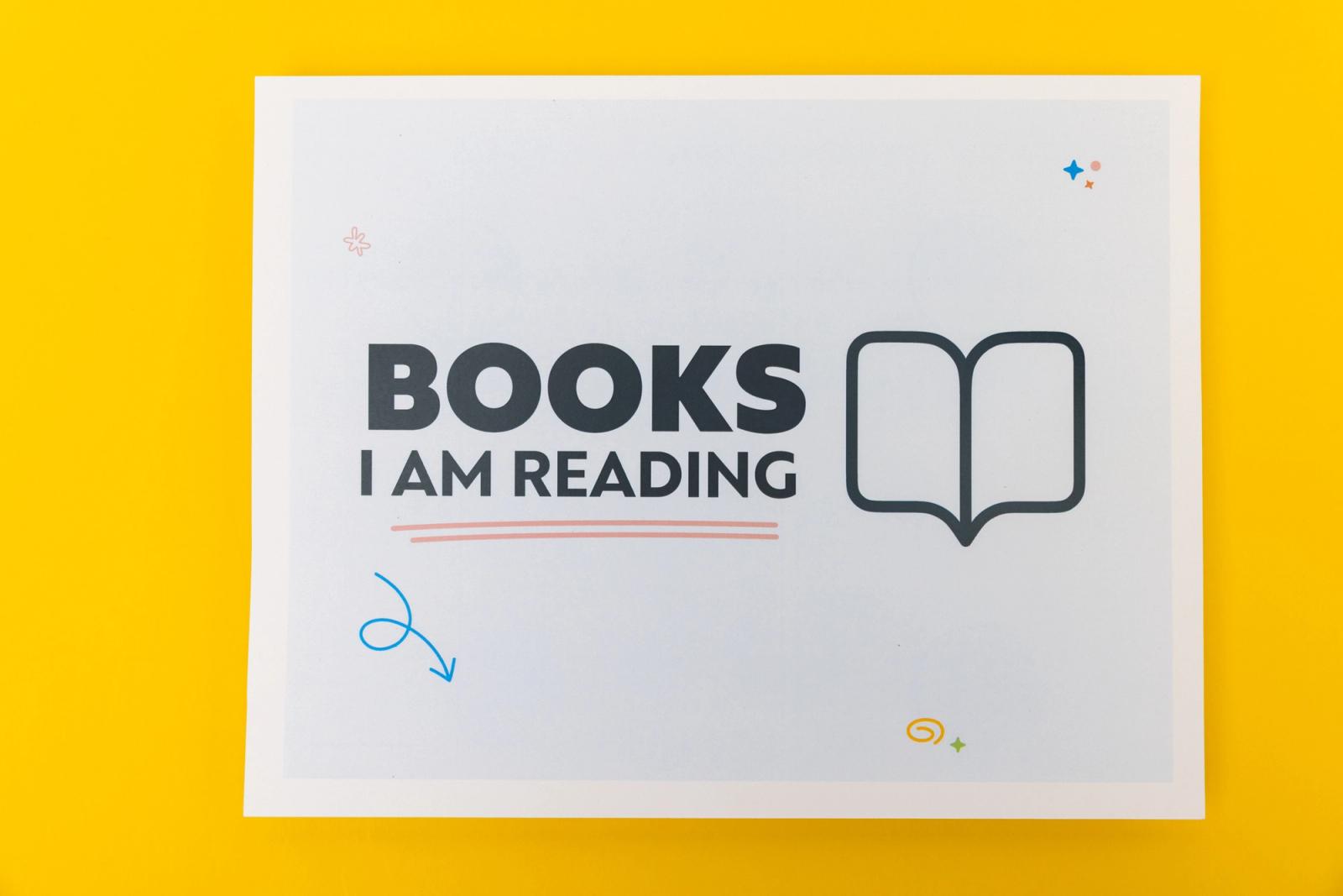 A piece of paper that says "books I am reading" lays on a yellow background.