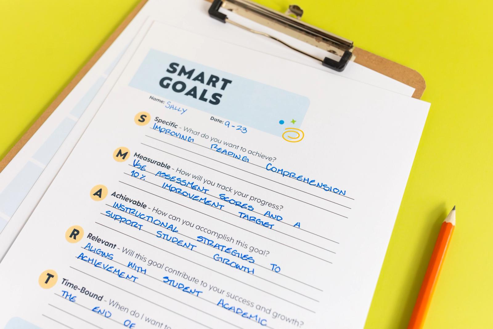 A clipboard with a sheet of paper that says "smart goals" and writing on it lays on a bright green background. An orange pencil lays beside the clipboard.