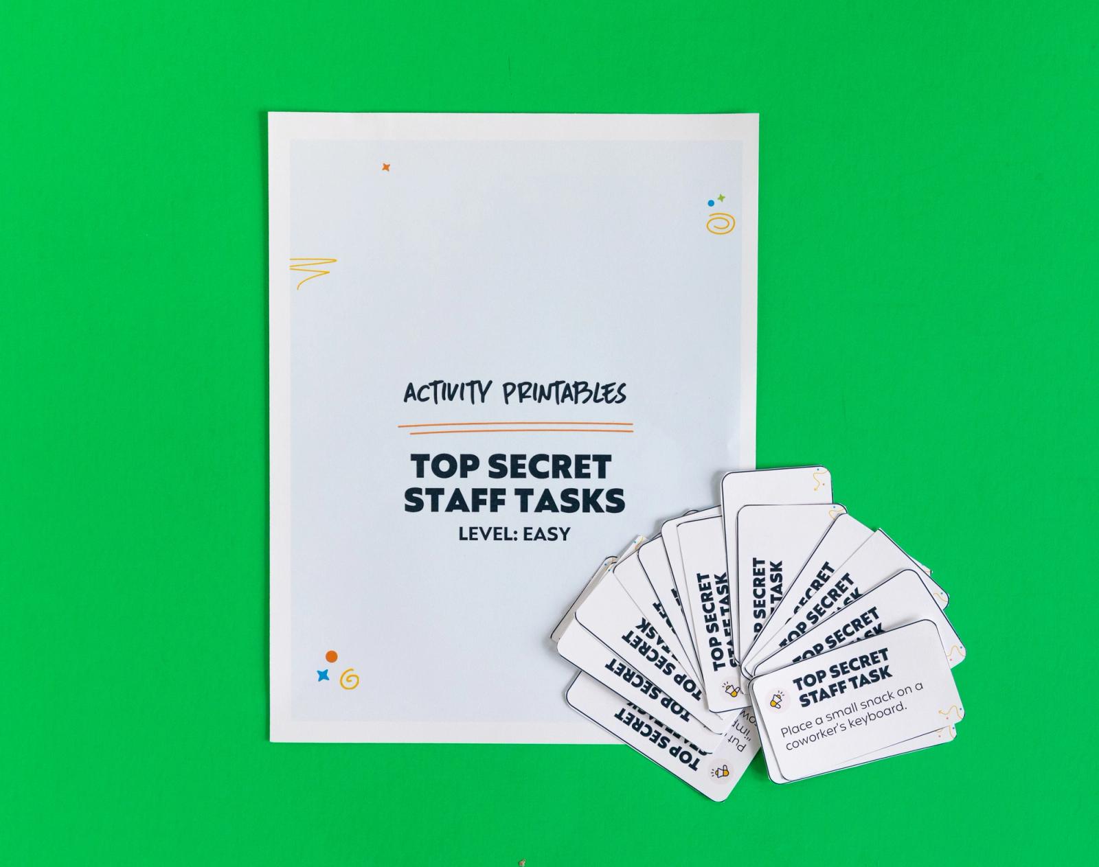 A sheet of paper that says "top secrete staff tasks: level: easy" lays on a green background. Small notecards lay beside it.