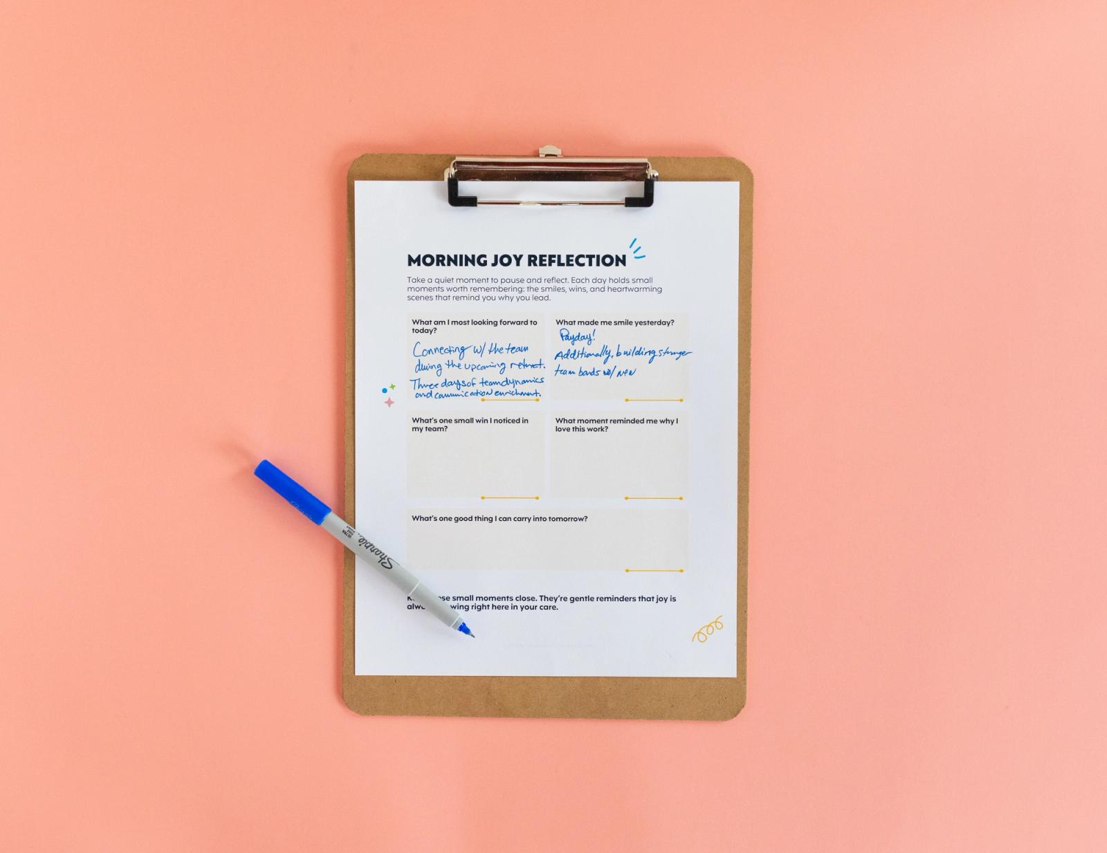 Sheet of paper on a clipboard and a blue pen lay on a salmon background.