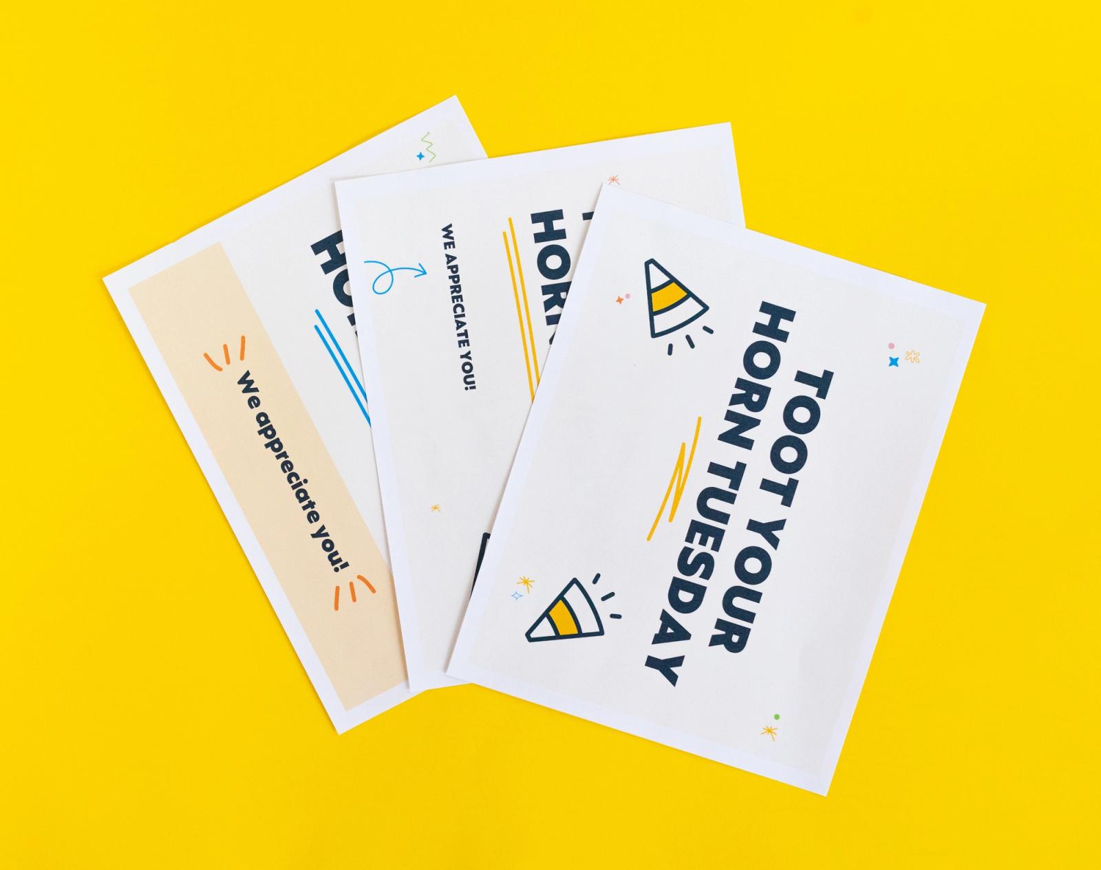 Three posters that say "toot your horn tuesday" lay fanned out on a yellow background.