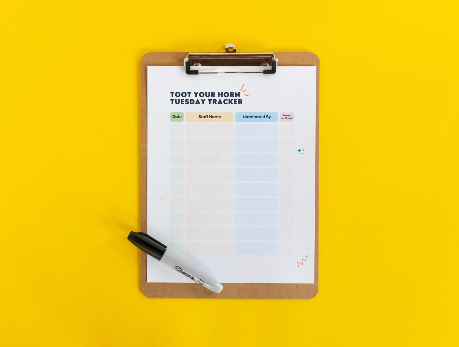 A clipboard with a sheet of paper that says "toot your horn tuesday tracker" on it lays on a yellow background.