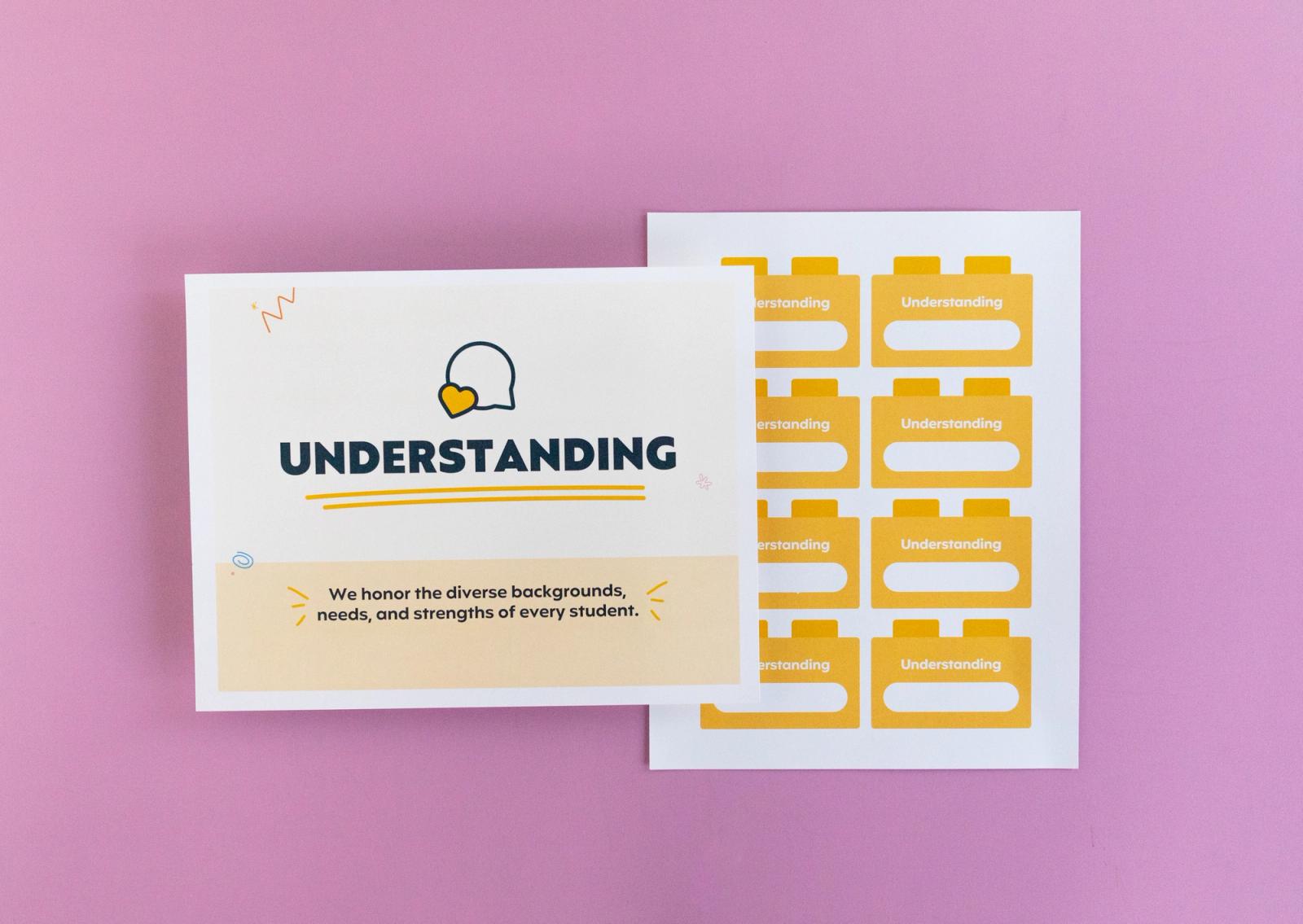 Sheet of paper that says "understanding" and another with small squares on it lay on a pink background.
