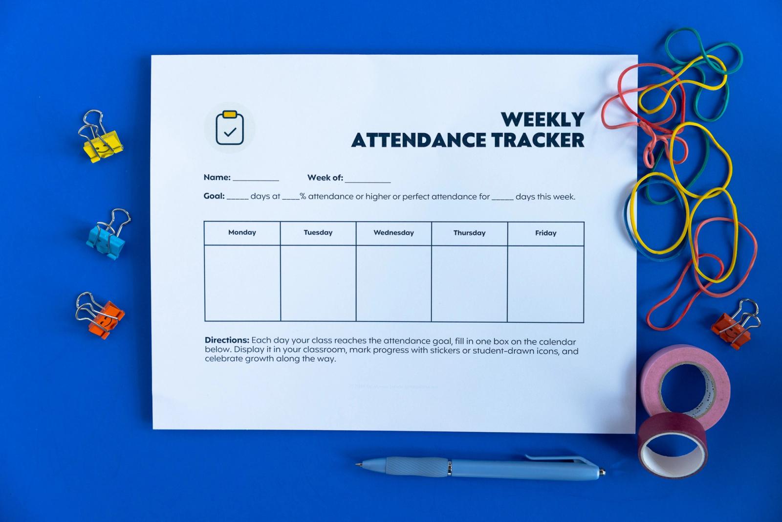 A sheet of paper that says "weekly attendance tracker" lays on a blue background. Paper clips, rubber bands, pens, and rolls of tape lay scattered around.