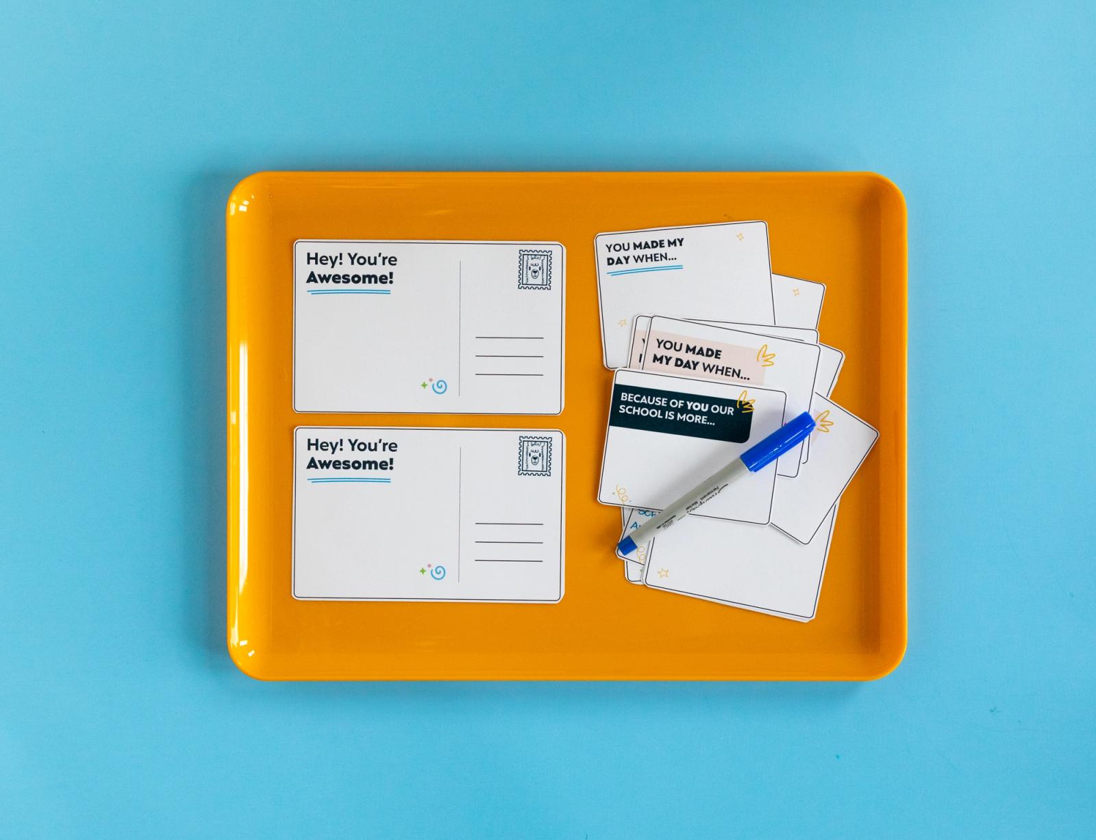 Small notecards and a blue pen lay on an orange tray on a light blue background.