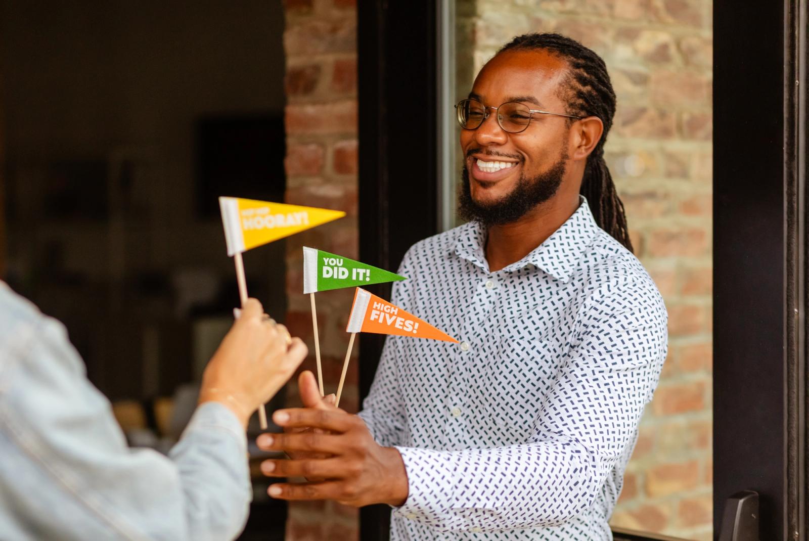 A man holds celebrate flags outside a door and hands one to someone.