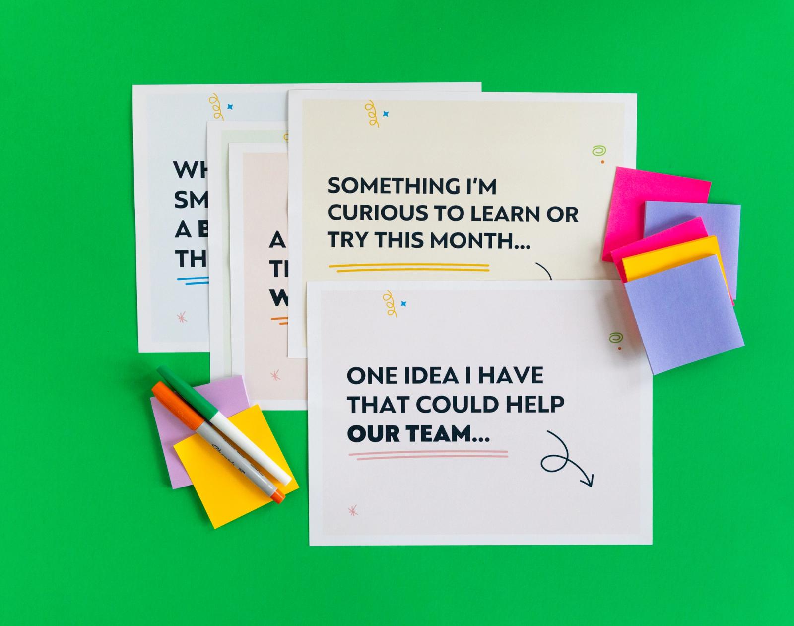 A pile of papers lay on a bright green background. Colorful sticky note pads and makers lay around them.