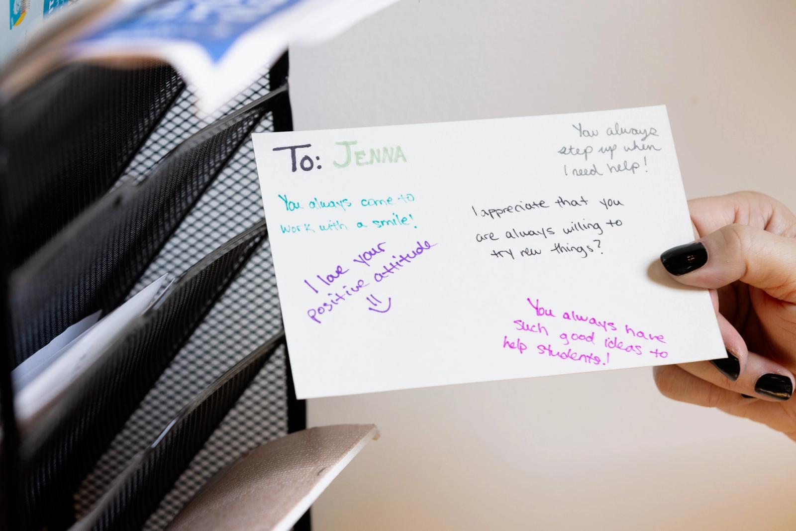 A hand places a notecard with handwritten notes on it in a slot mailbox.