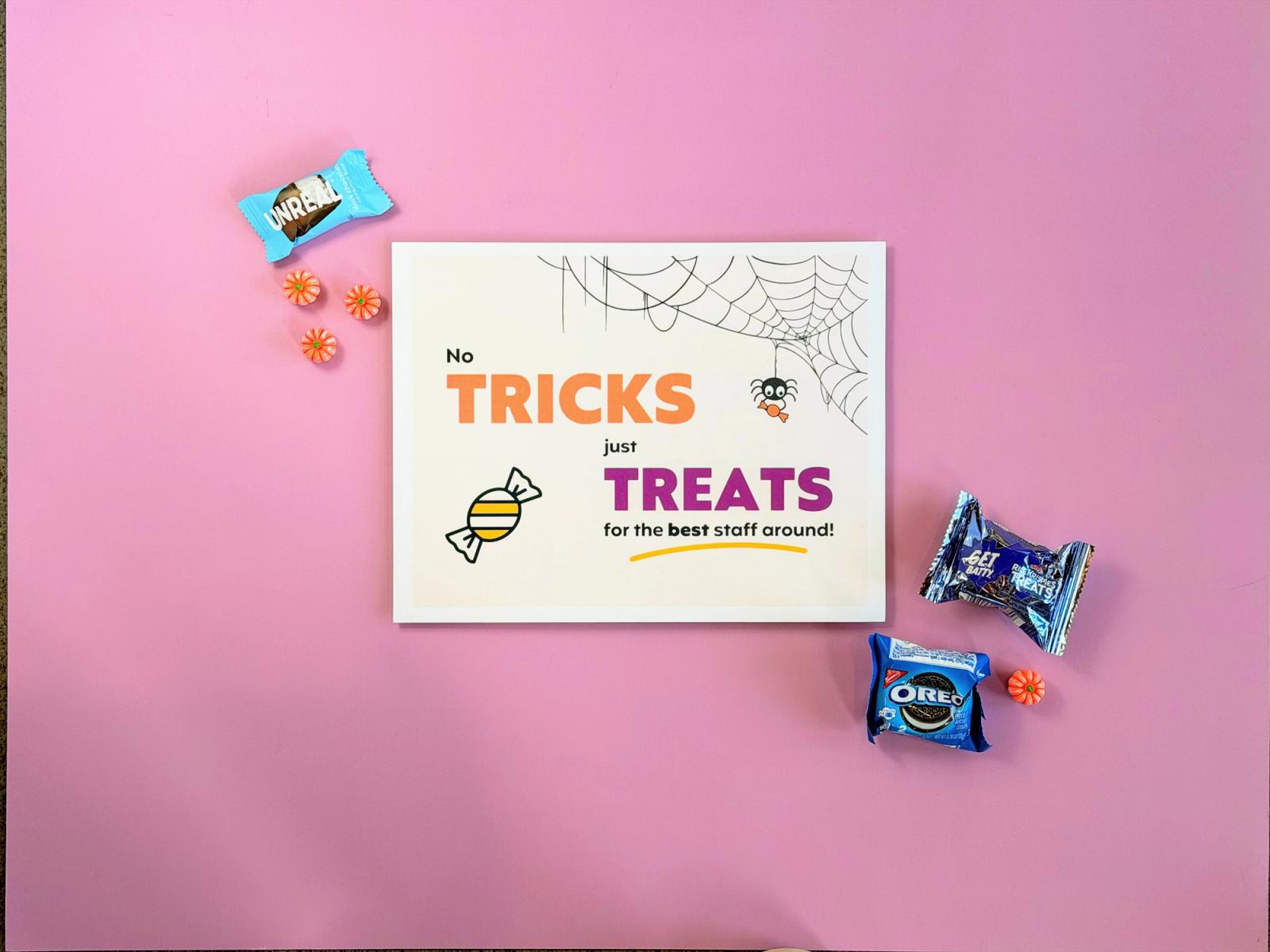 “No tricks, just treats” staff trick or treat sign surrounded by wrapped cookies, chocolate, and pumpkin candies