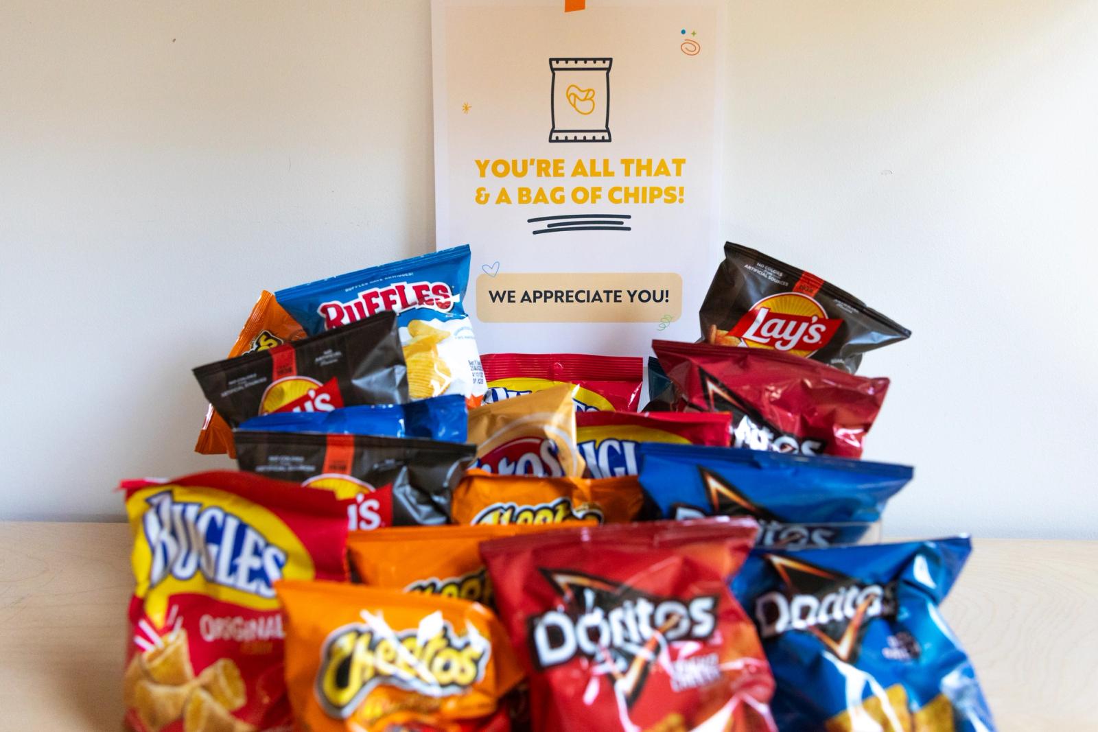 Small bags of chips are on a table in front of a poster that says "you're all that and a bag of chips" behind it.